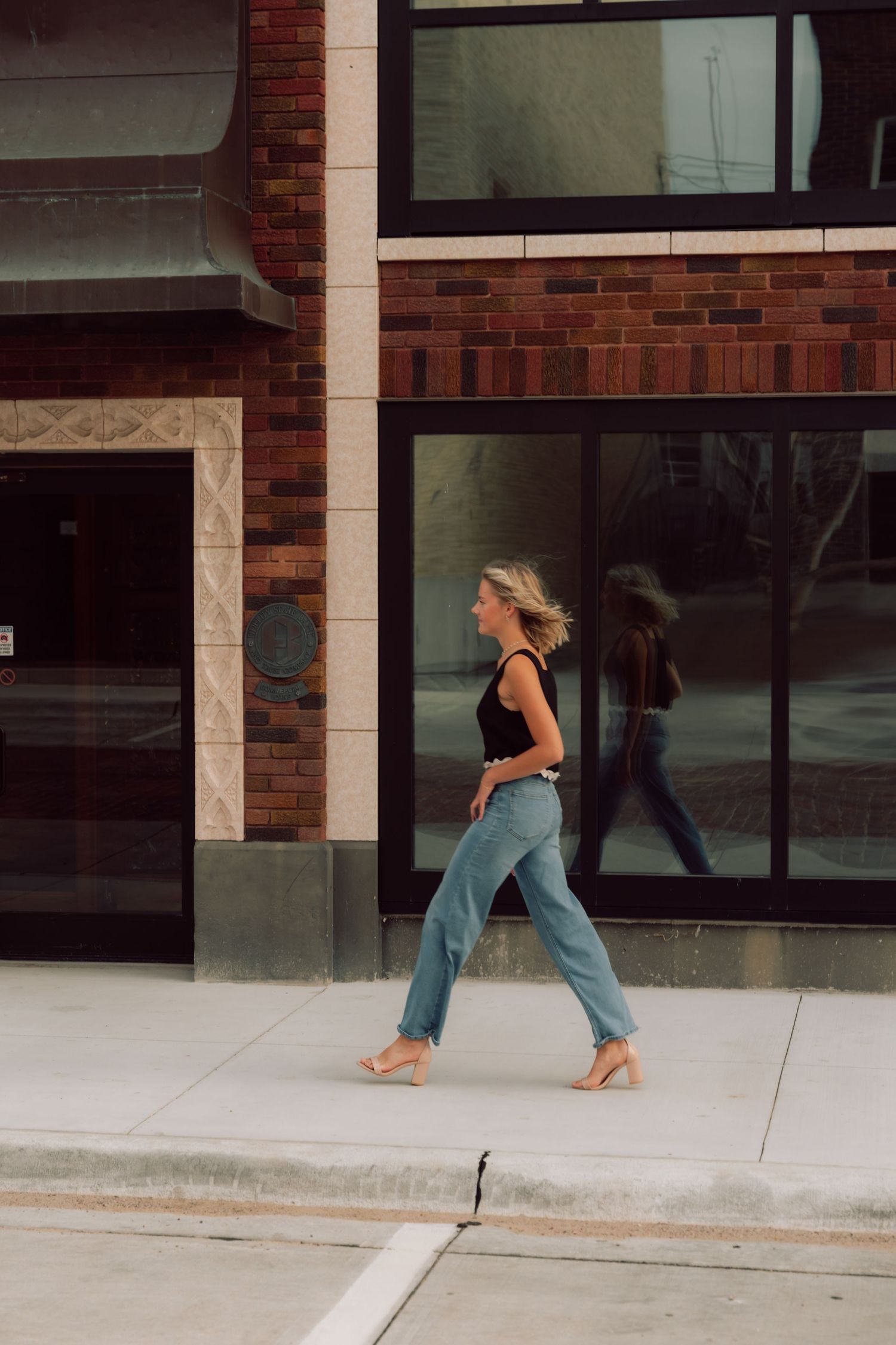 Person in motion captured along a brick building facade with concrete sidewalk.