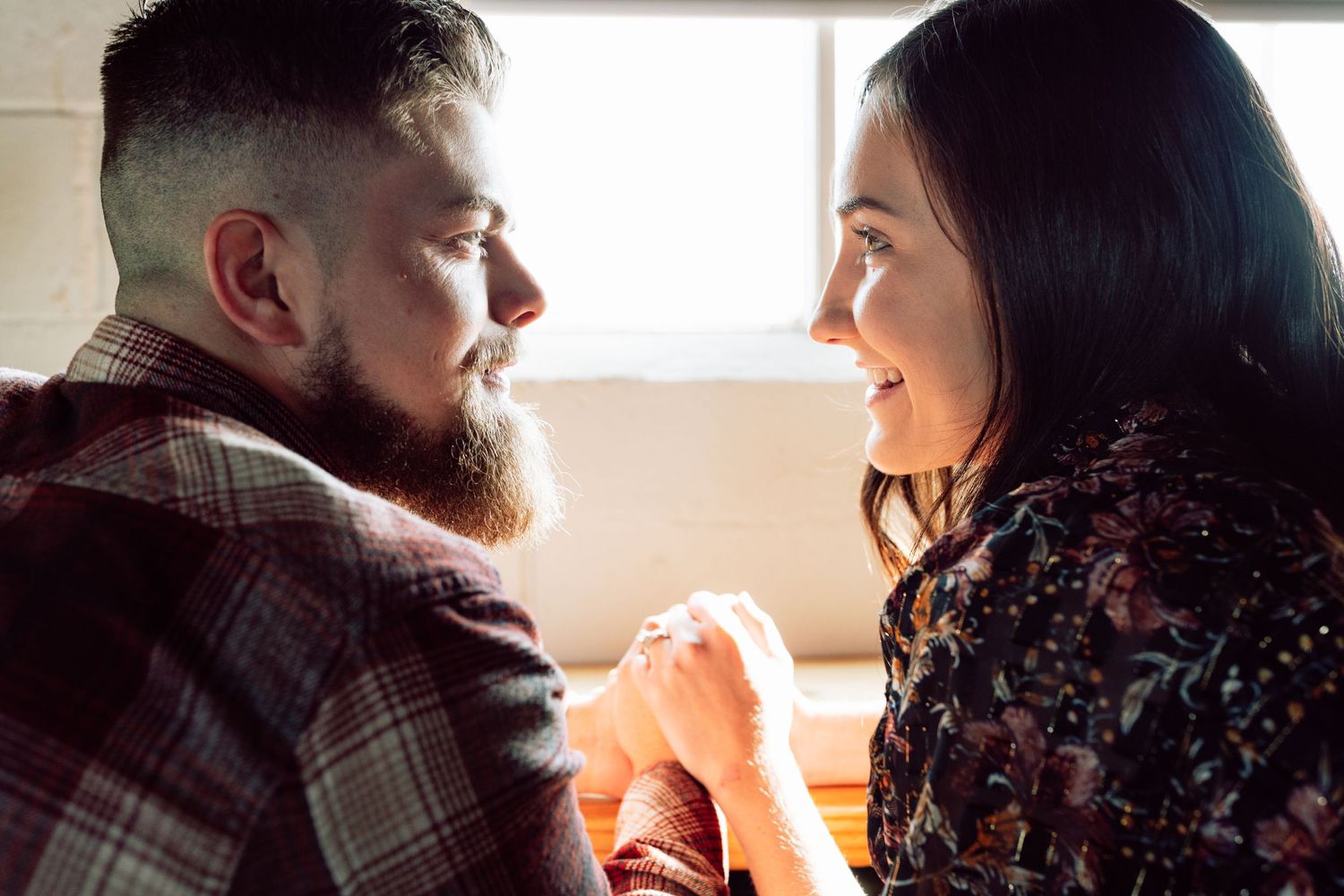 Romantic couple embracing in soft window light against wooden wall backdrop.