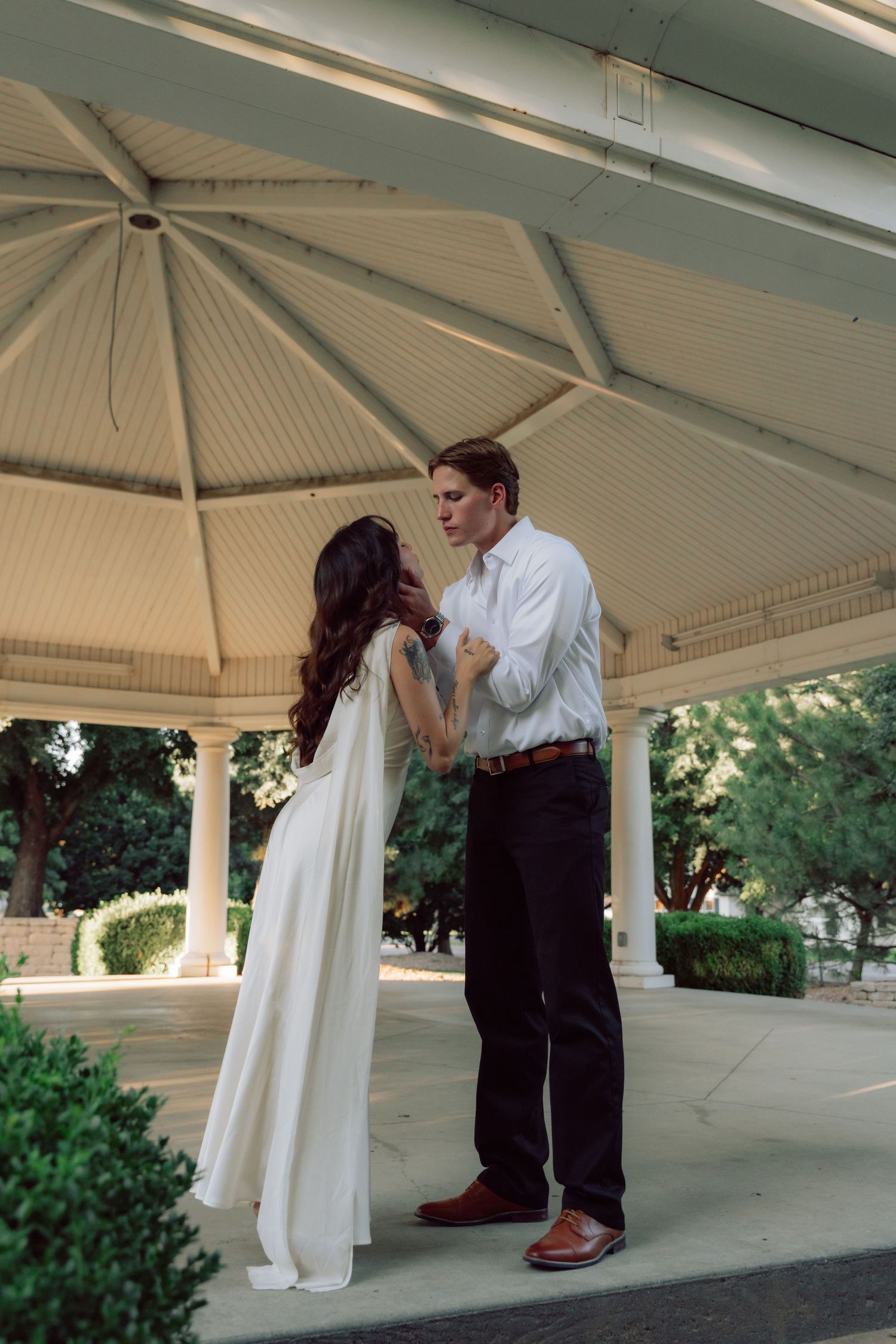 A tender moment between a couple in a white gazebo with architectural details.