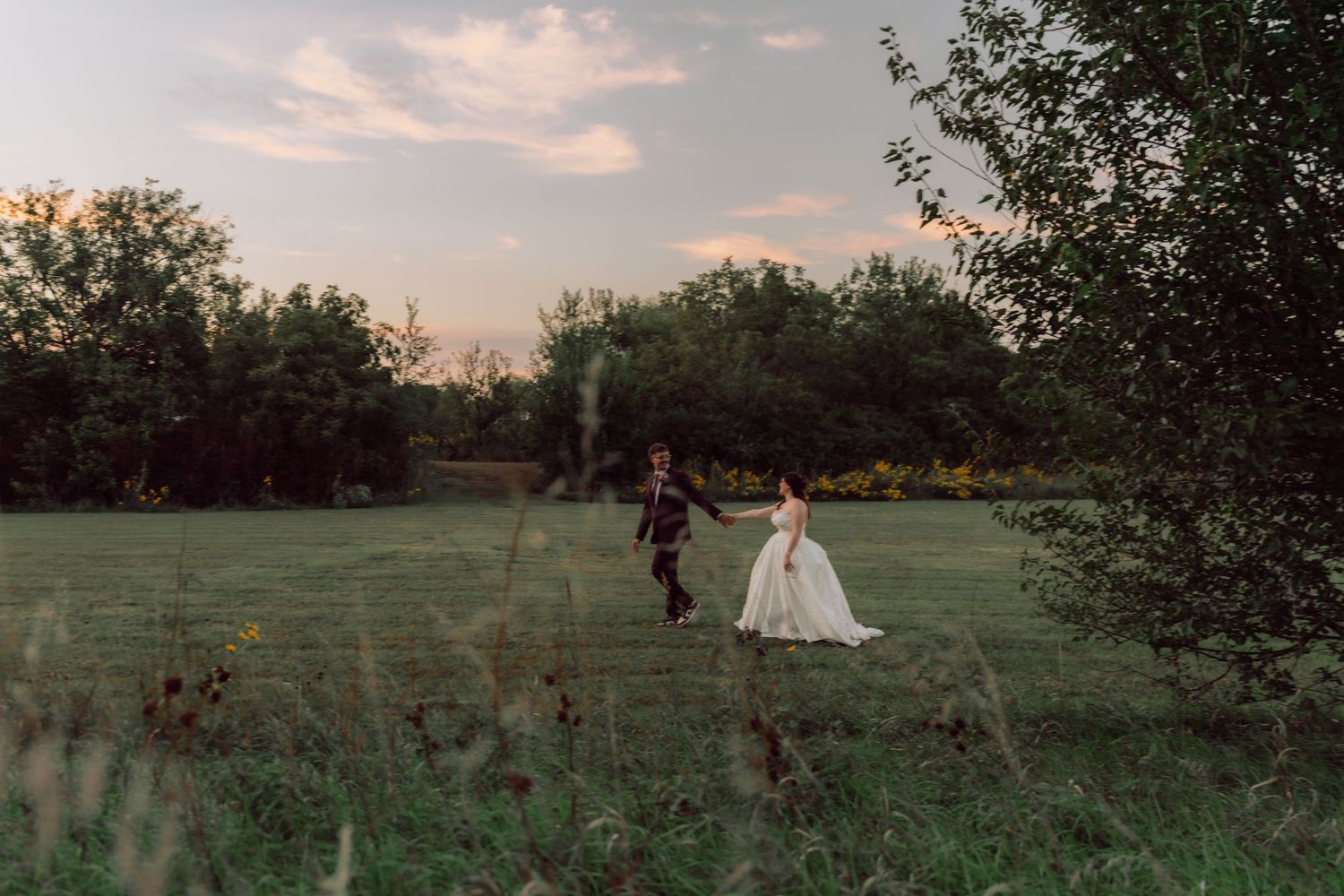 Silhouettes of a wedding couple embrace in a golden field during sunset.