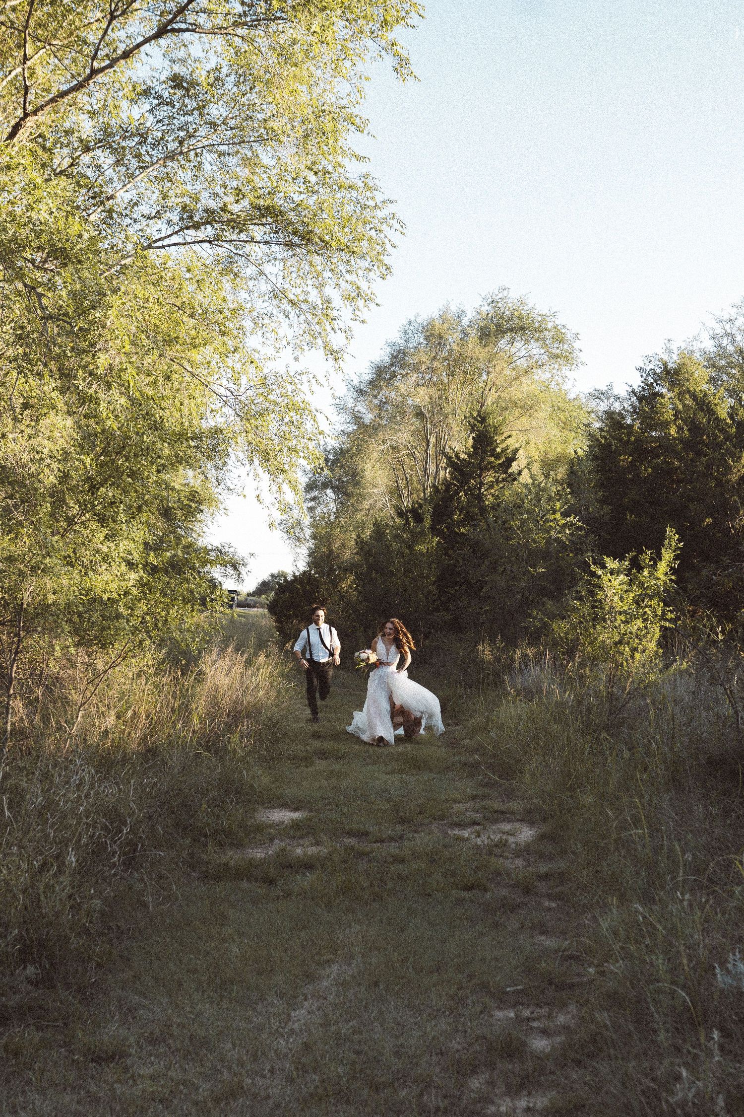Two people walk along a winding dirt path through green foliage.