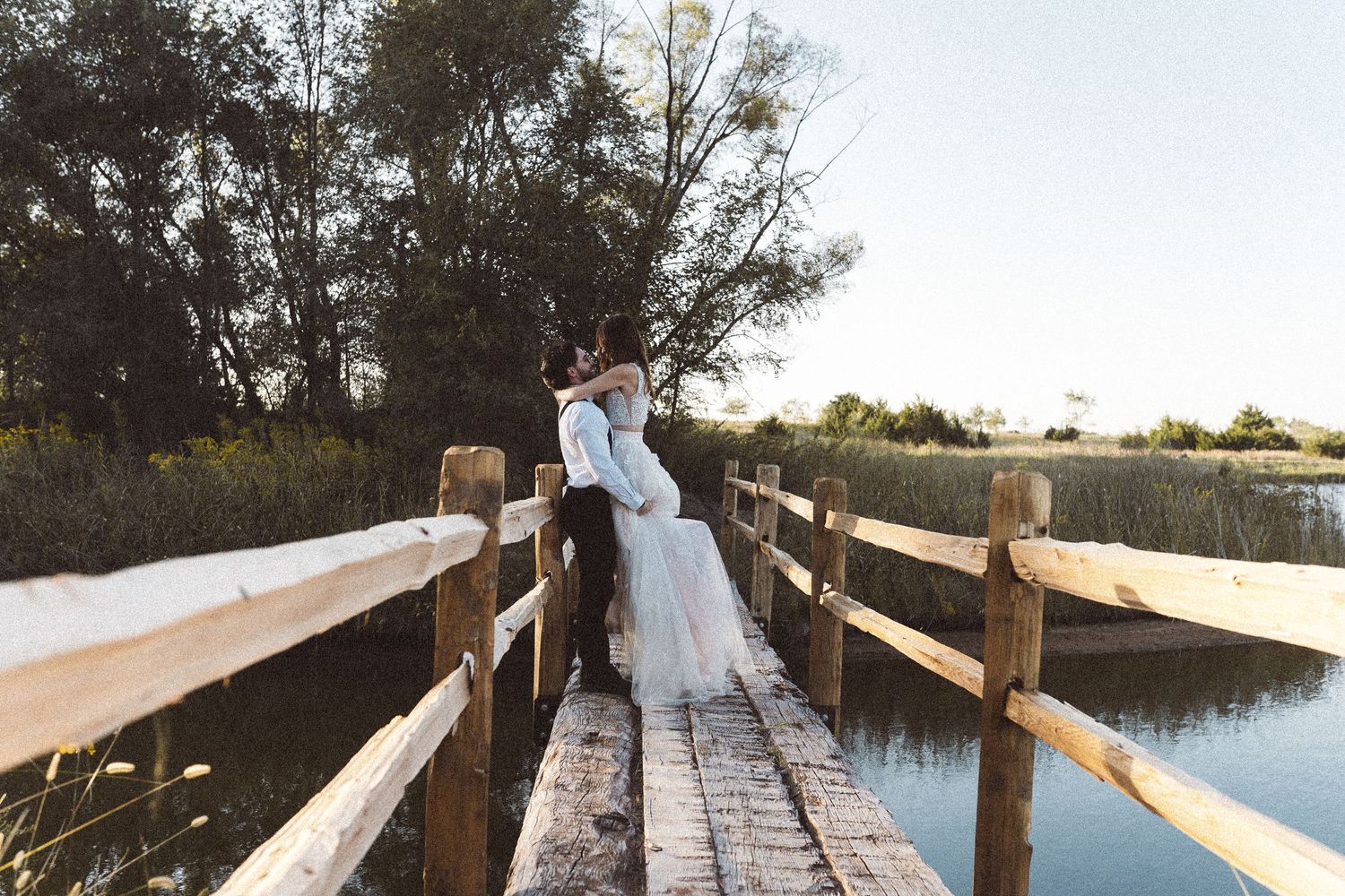 Two people walk together on a wooden bridge over calm water during sunset.