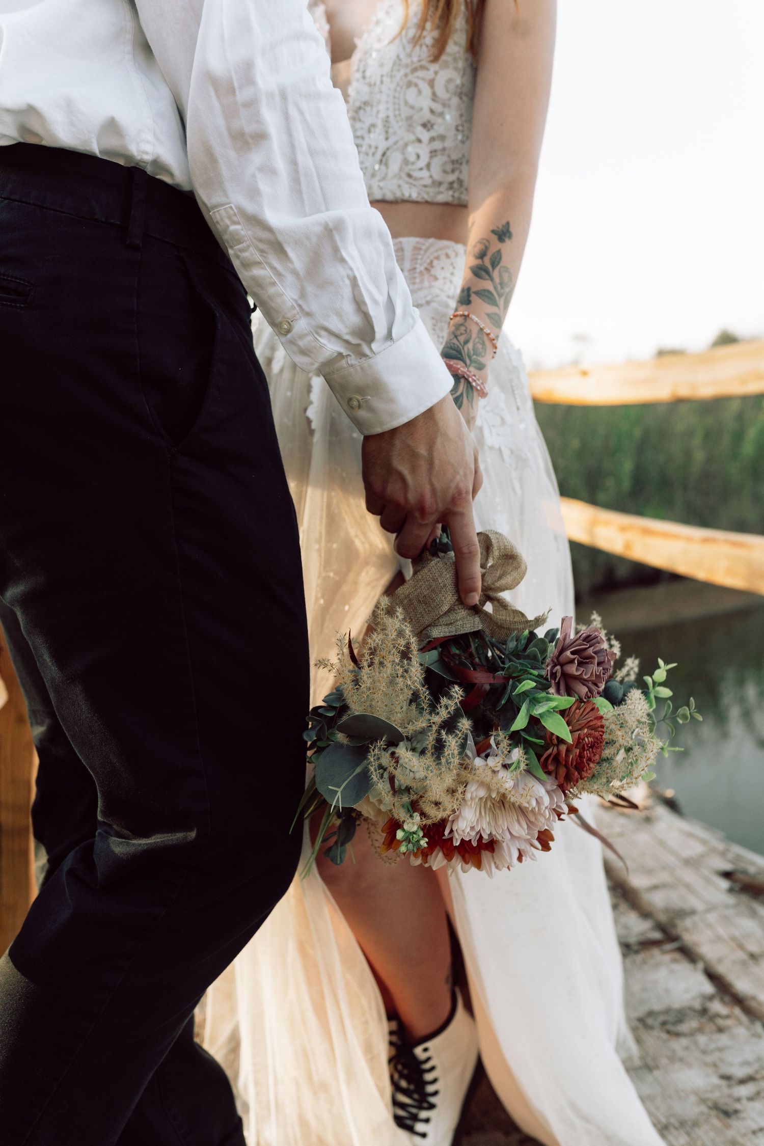 Wedding bouquet with burgundy and white flowers held against flowing white dress.