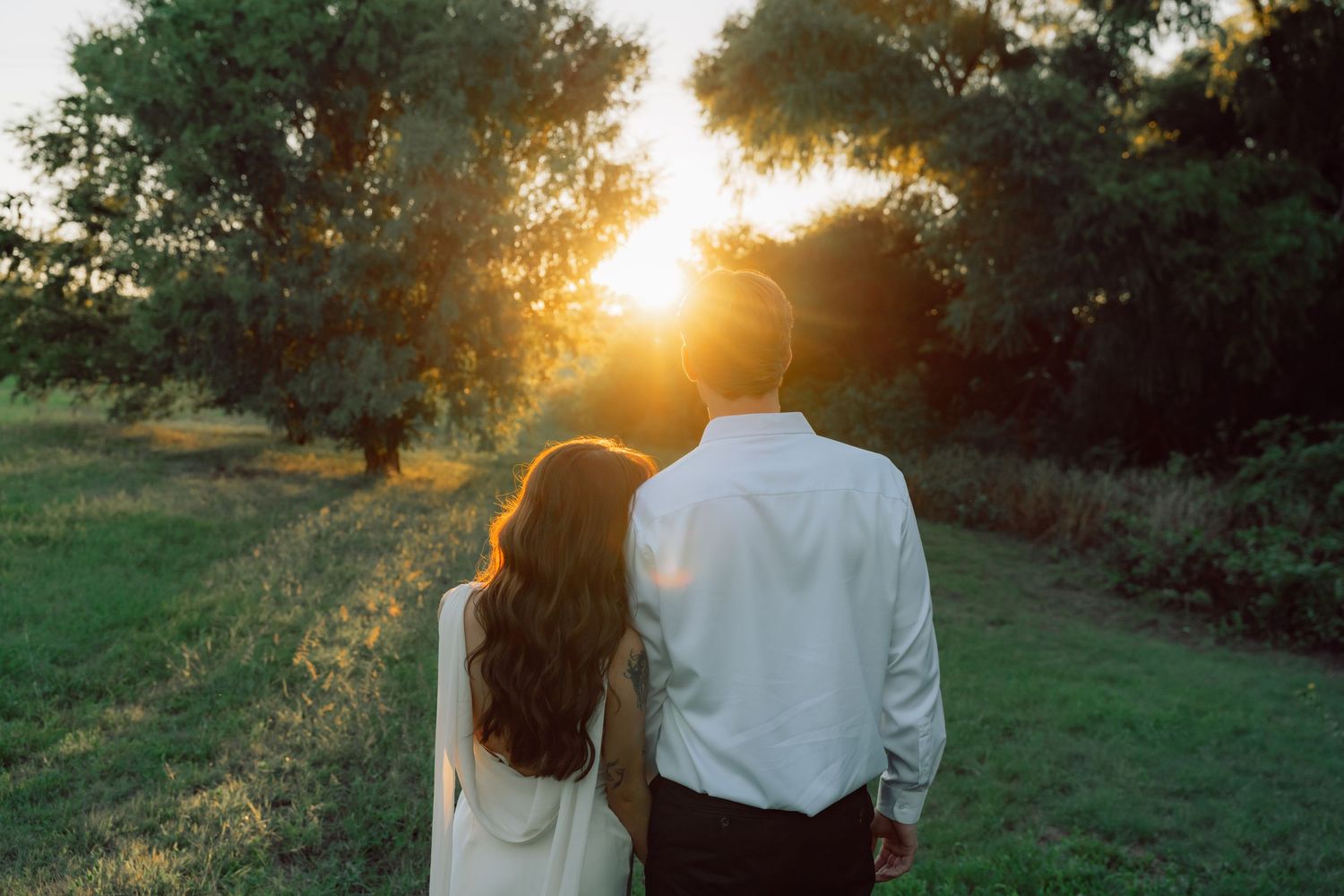 A romantic moment captured in a grassy field with dramatic sunset lighting and trees.