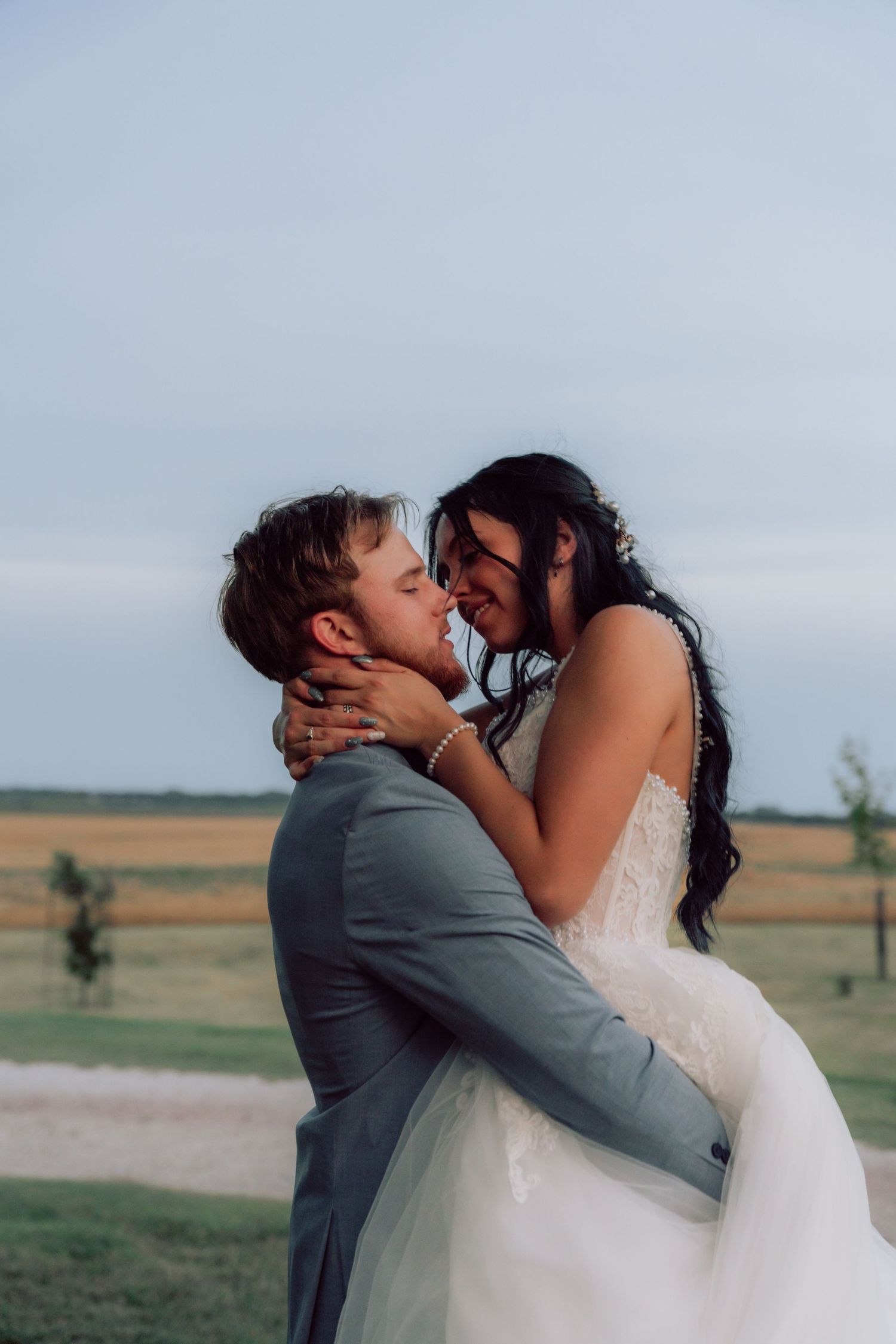 Intimate wedding portrait shows couple sharing a tender kiss against a rural landscape.
