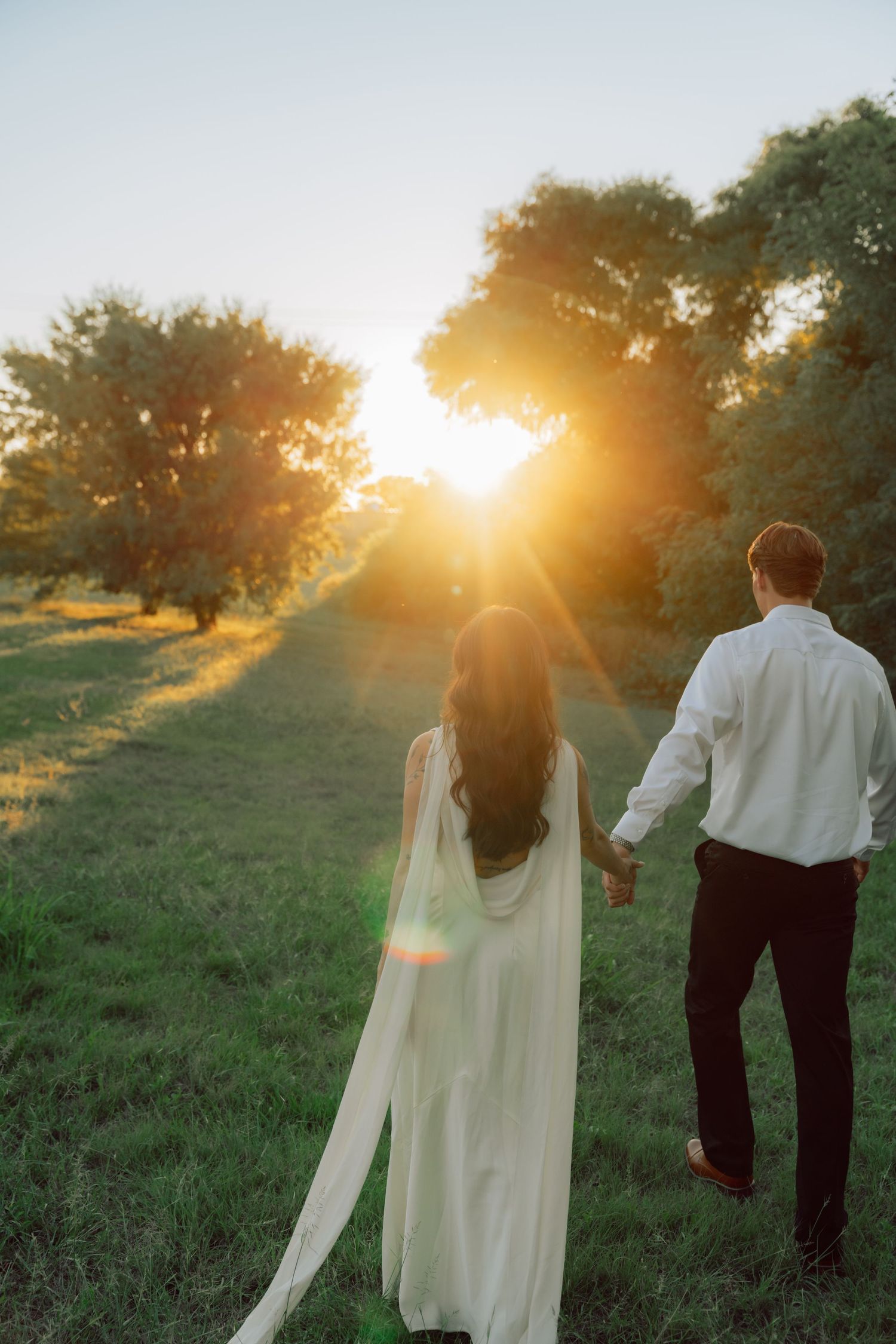 A couple walks hand in hand during sunset in a grassy field.