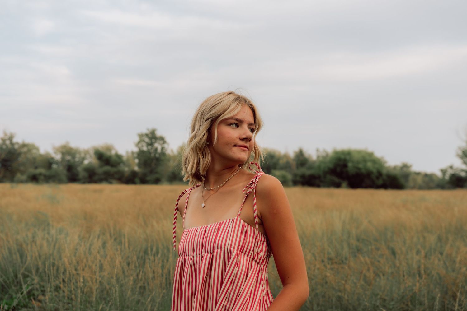Person in striped sundress poses against a natural landscape with trees in background.
