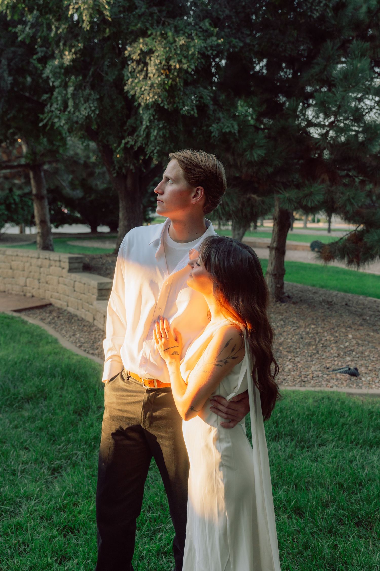 A couple in white and brown outfits share an intimate moment in a garden setting.
