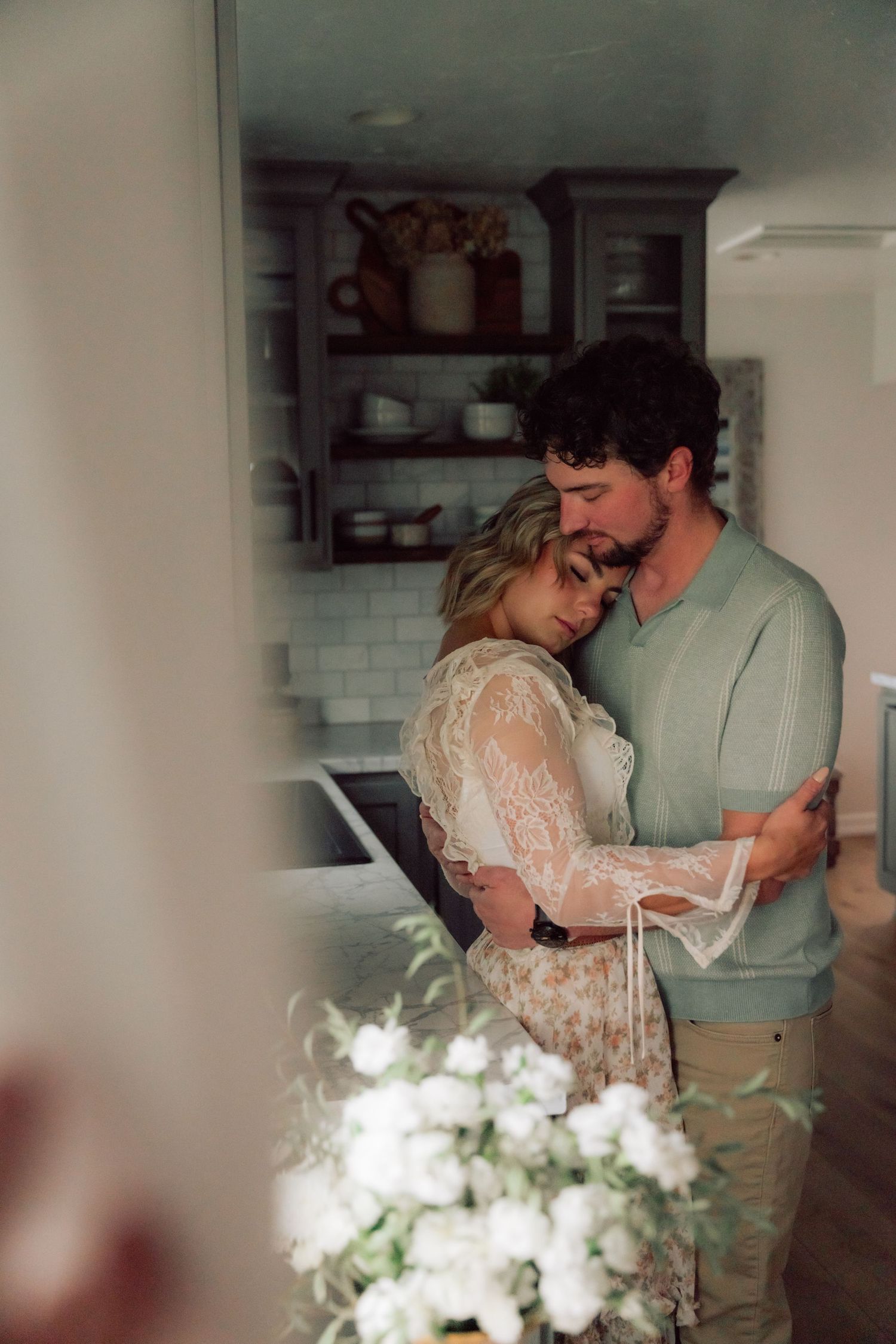 A tender moment between a couple in a cozy kitchen with white flowers in the foreground.