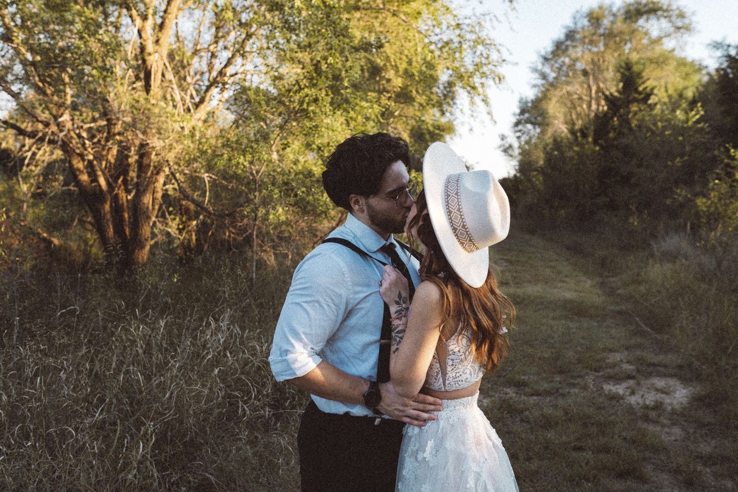 Newlyweds share a tender moment while walking along a sunlit nature path.