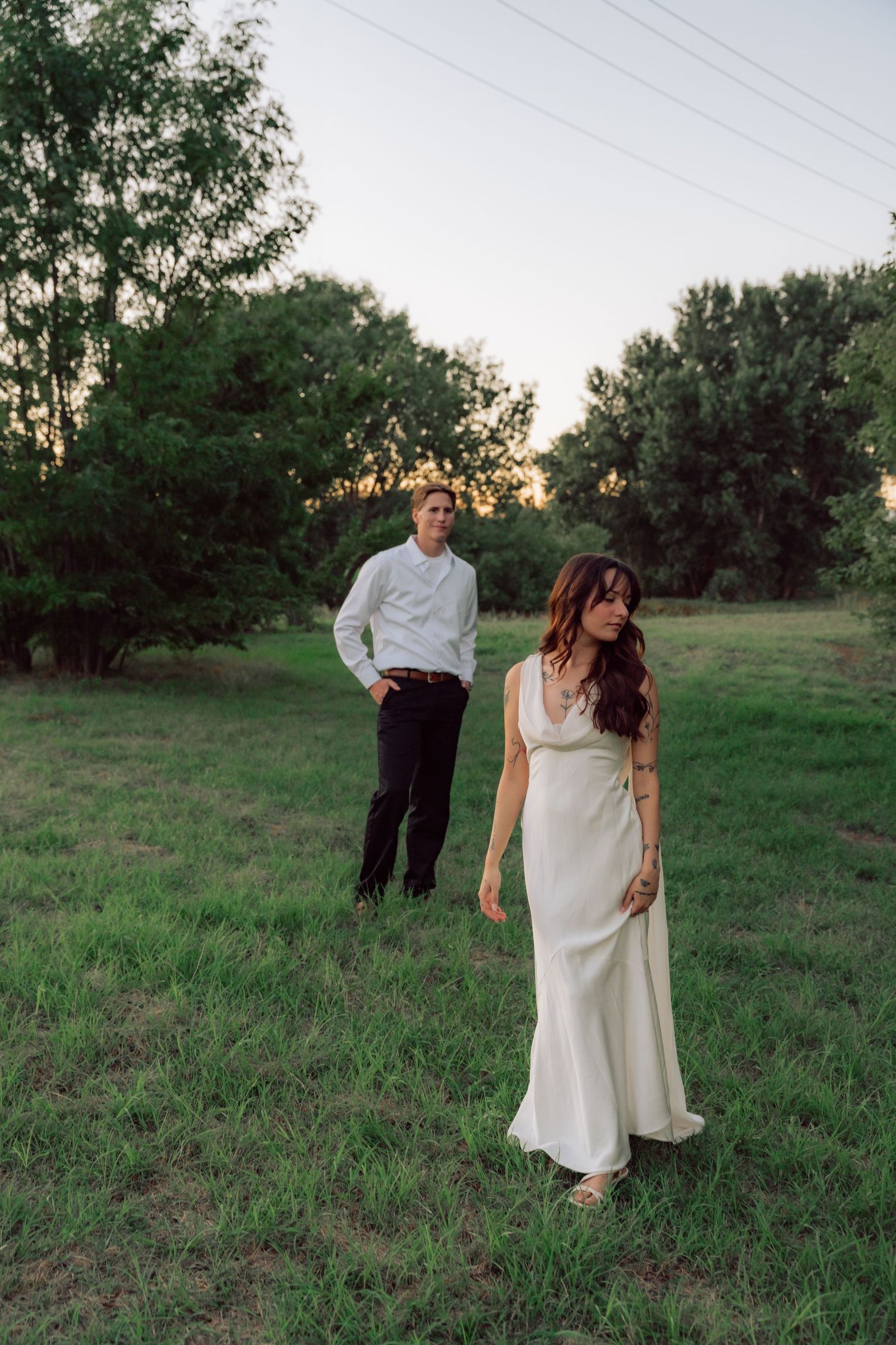 Two people walking together in a green field at sunset wearing formal attire.