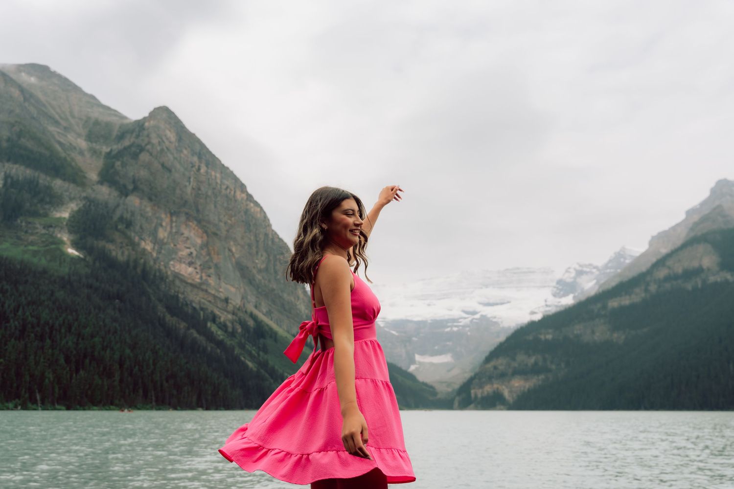 Dancing figure in bright pink dress twirls against mountain lake backdrop.