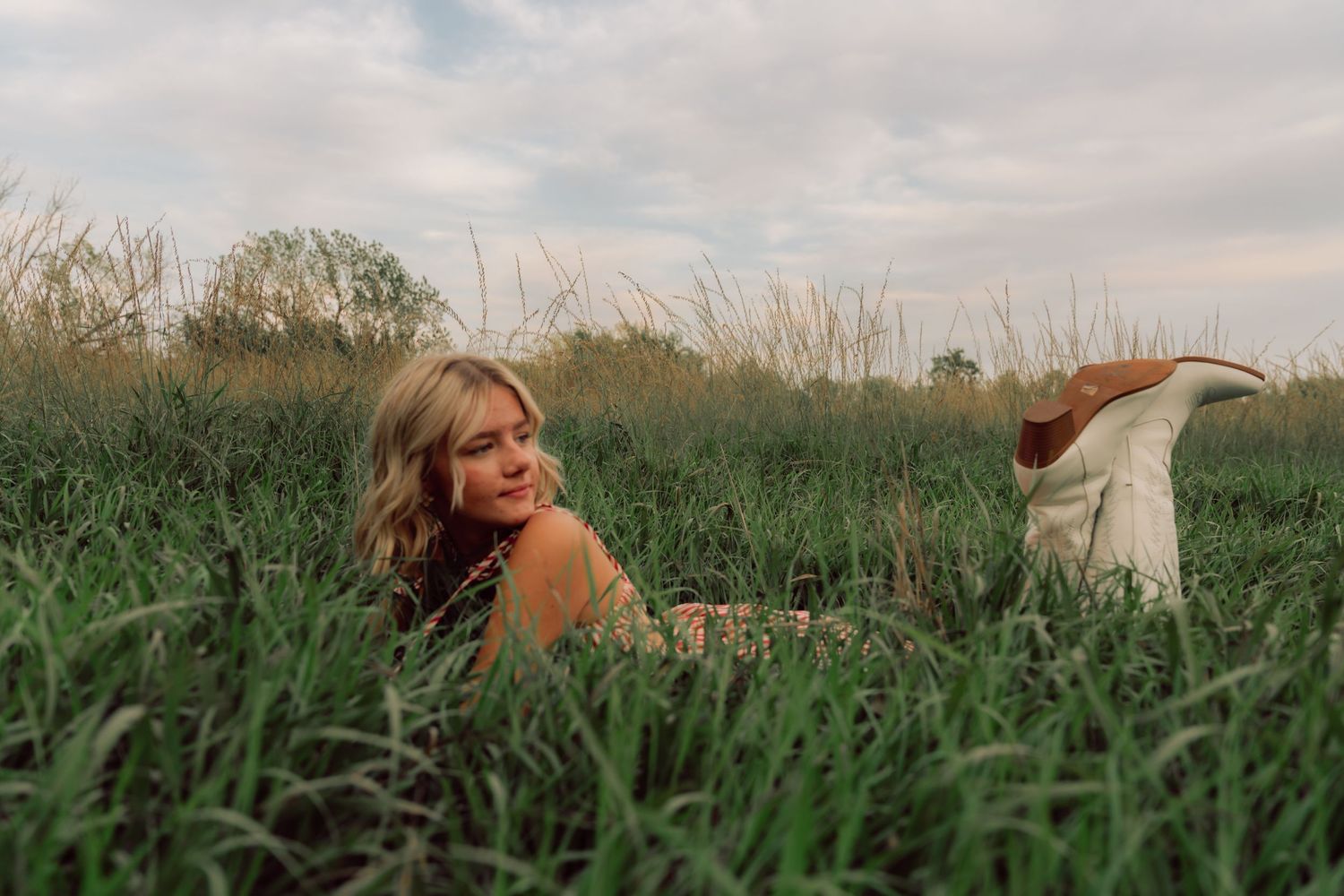 Figure lying in green grass wearing casual summer clothing on cloudy day.