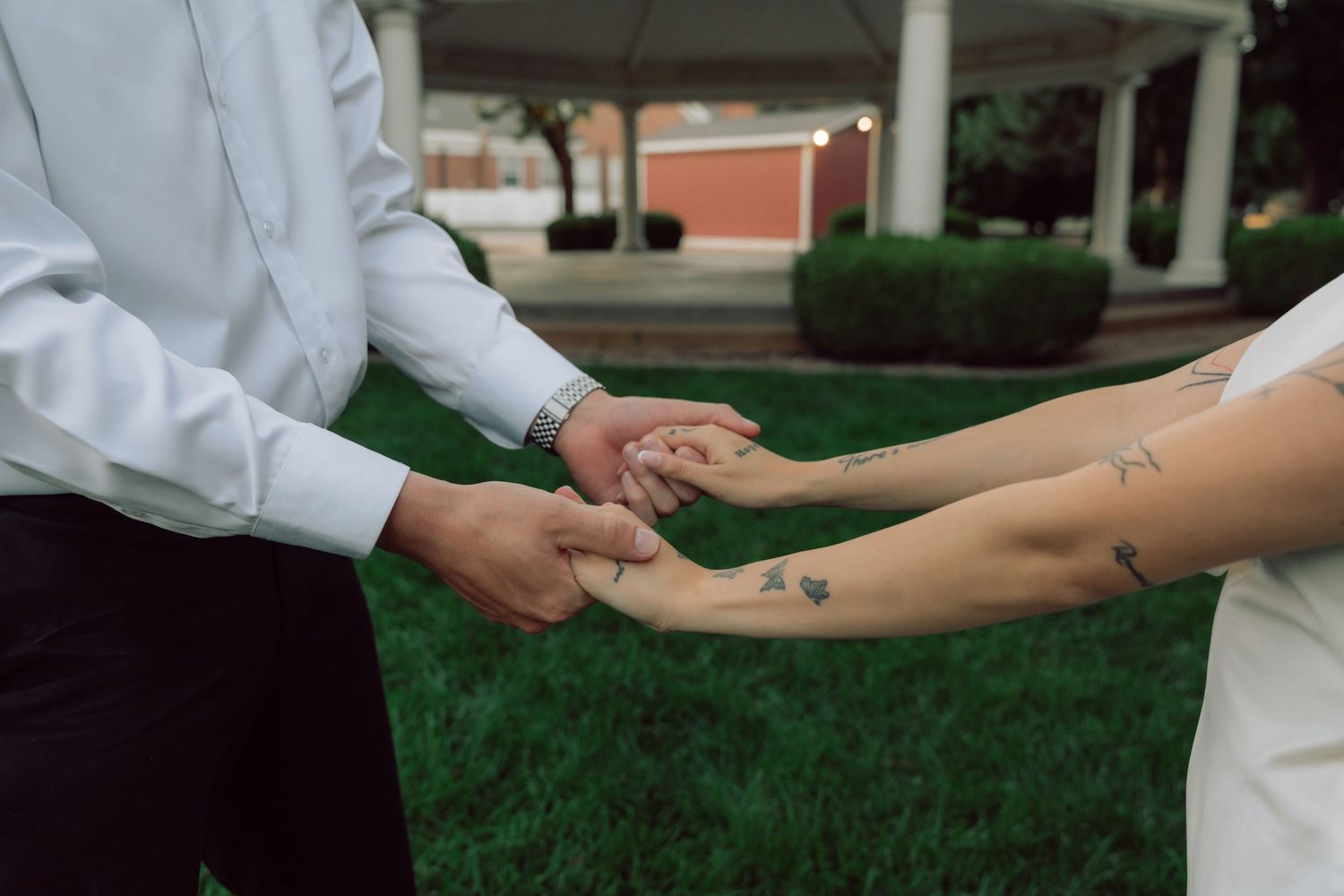 Two people holding hands in white clothing against a garden background.