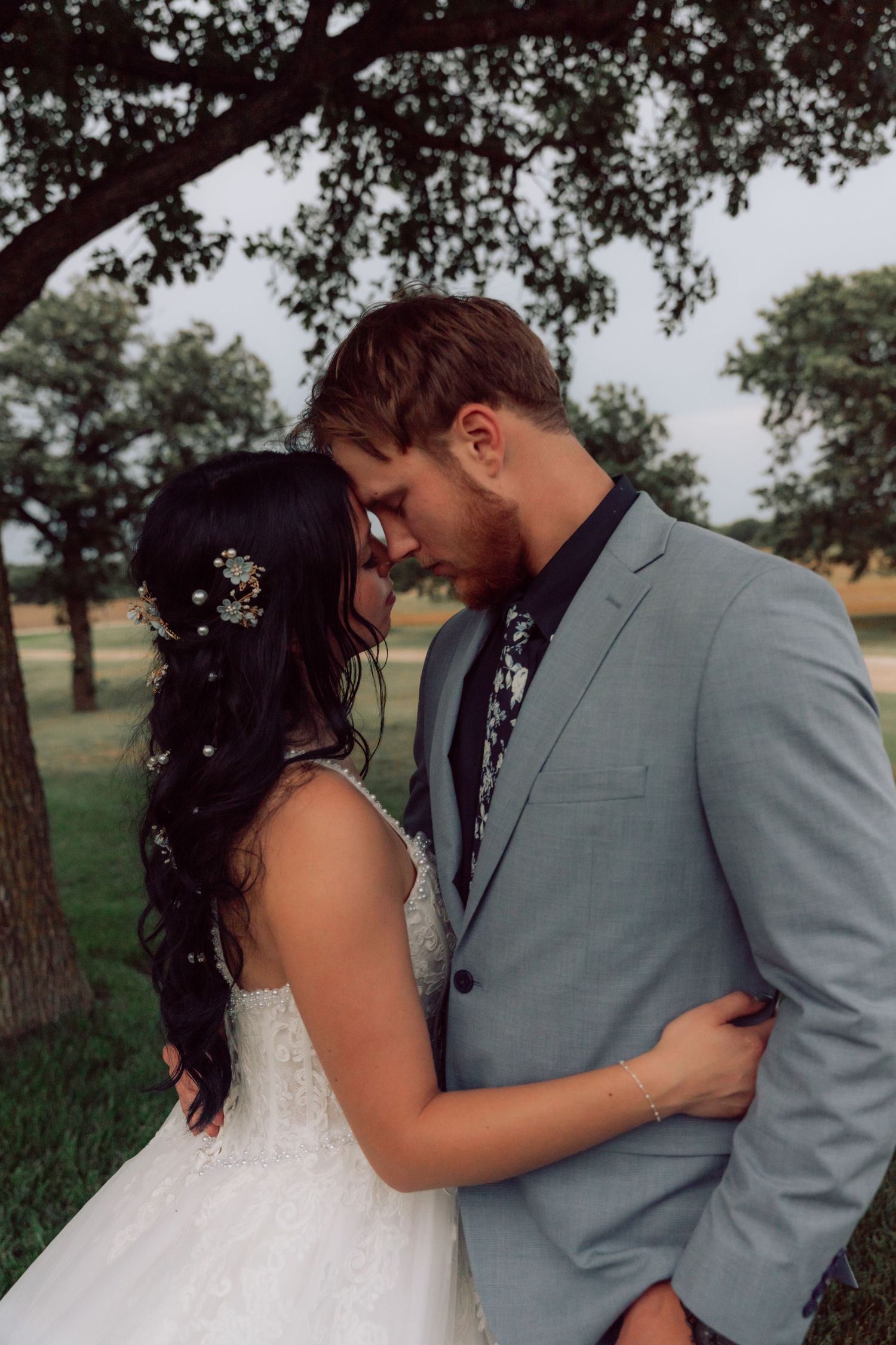 A romantic moment captured between newlyweds under a tree in soft lighting.