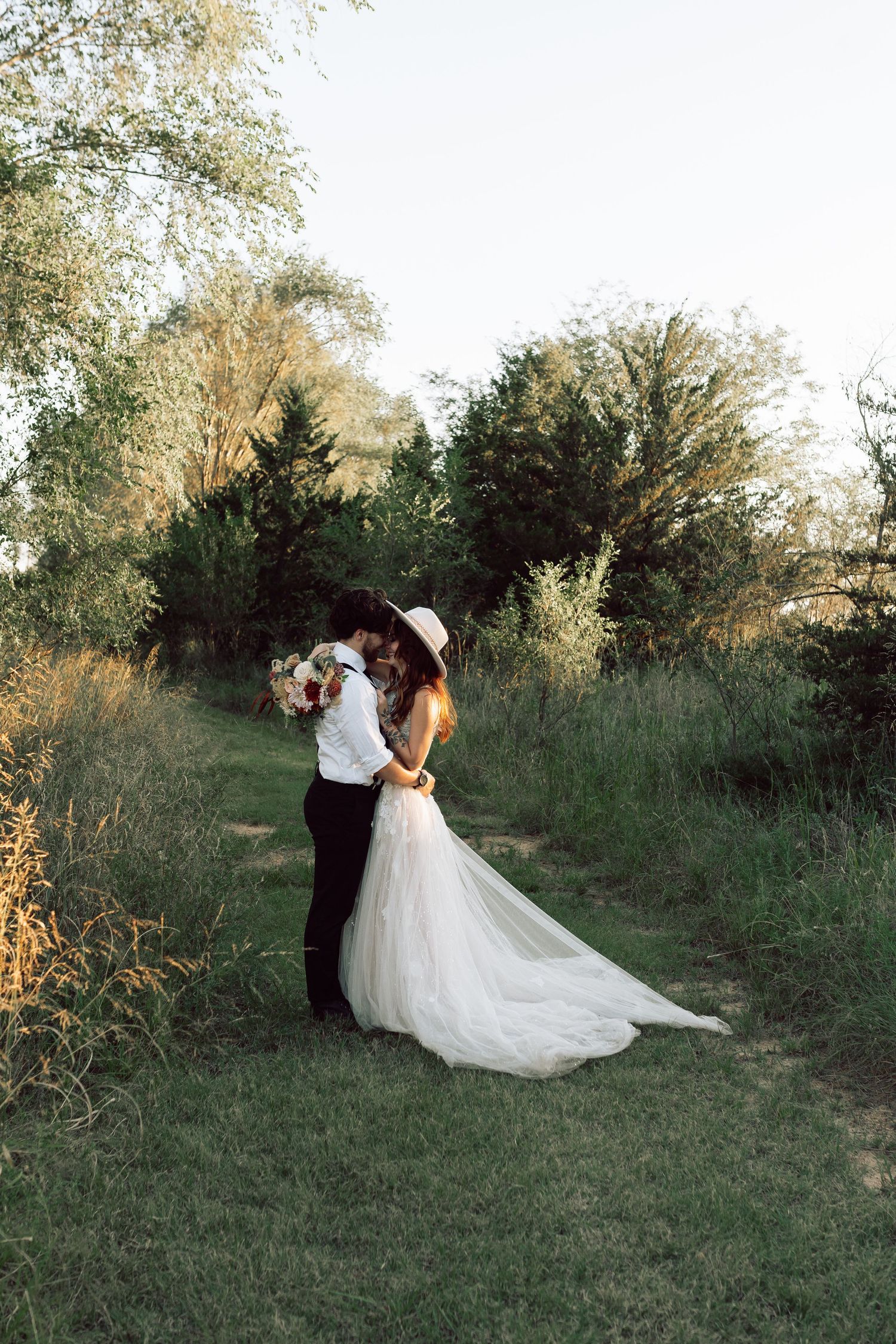 Newlyweds share an intimate moment on a rustic outdoor trail surrounded by greenery.