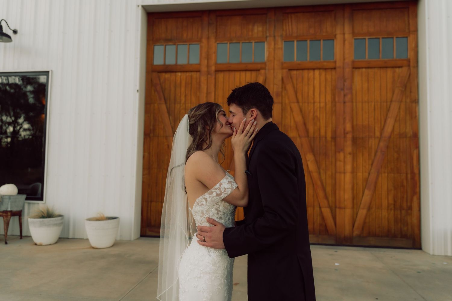 A tender moment between newlyweds against a white building with wooden doors.