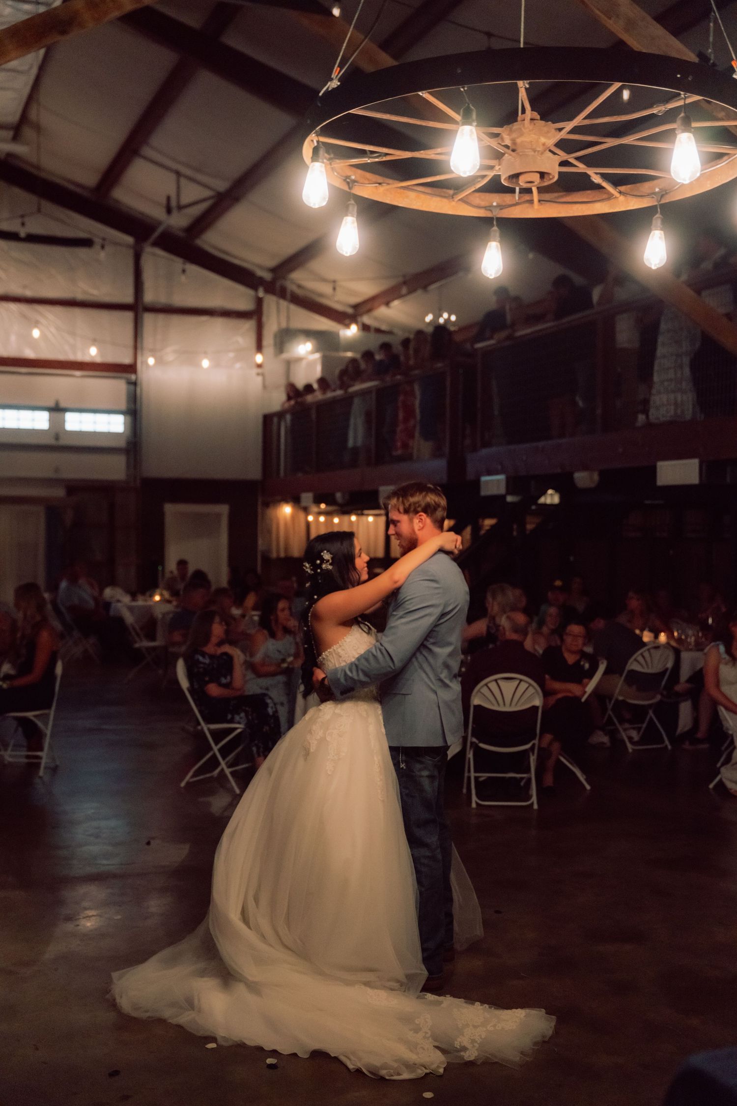 Couple shares their first dance under industrial chandelier lighting in a rustic venue.