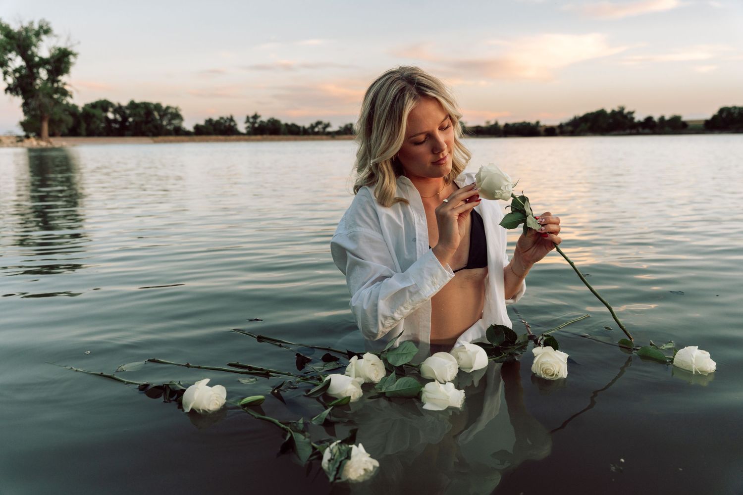 Person in water at sunset holding white flowers.