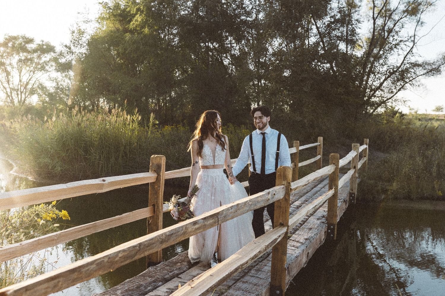 Couple shares a romantic moment on an old wooden bridge with water and trees in the background.
