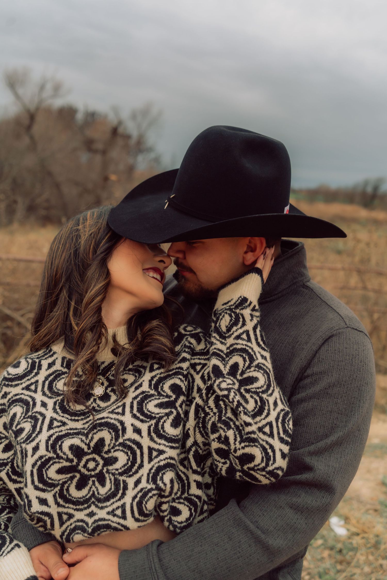 A romantic couple in western attire sharing an intimate moment in a rustic outdoor setting.