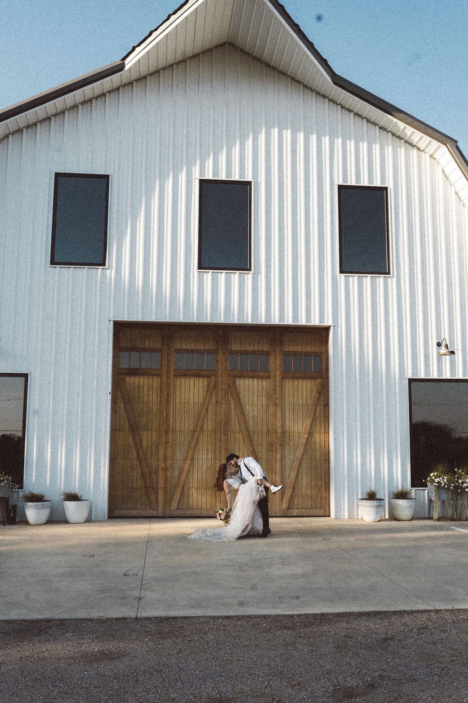 Exterior view of a white barn building with large wooden doors and black windows.