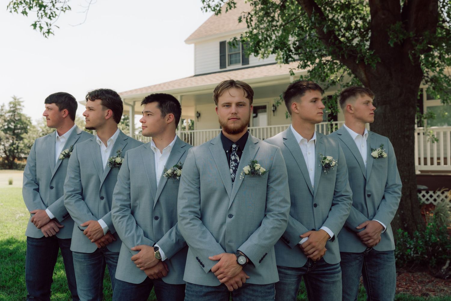 Wedding party groomsmen wearing matching gray suits pose together outside.