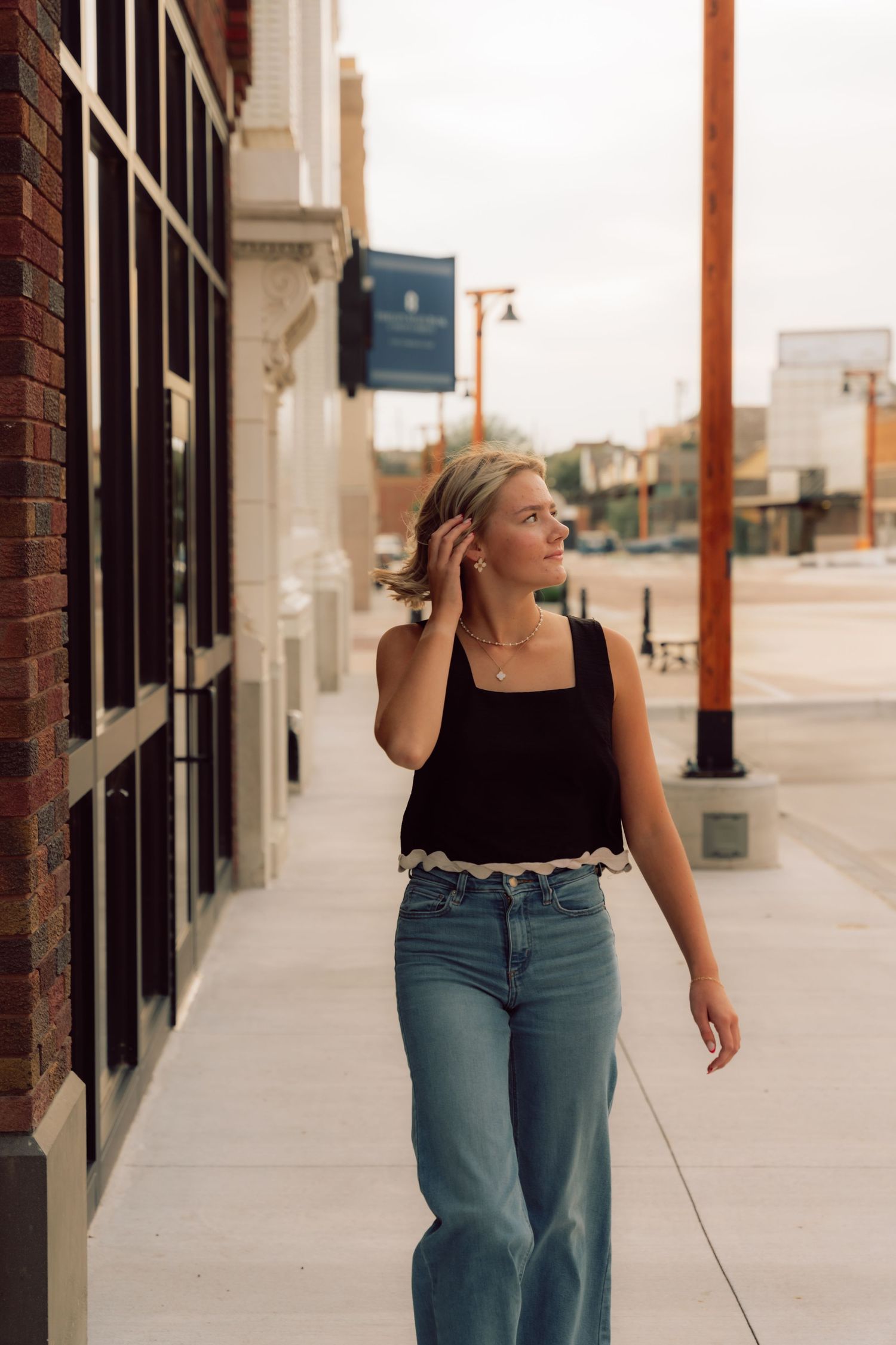 A casual outdoor photoshoot against a white brick building with blue jeans and a black tank top.