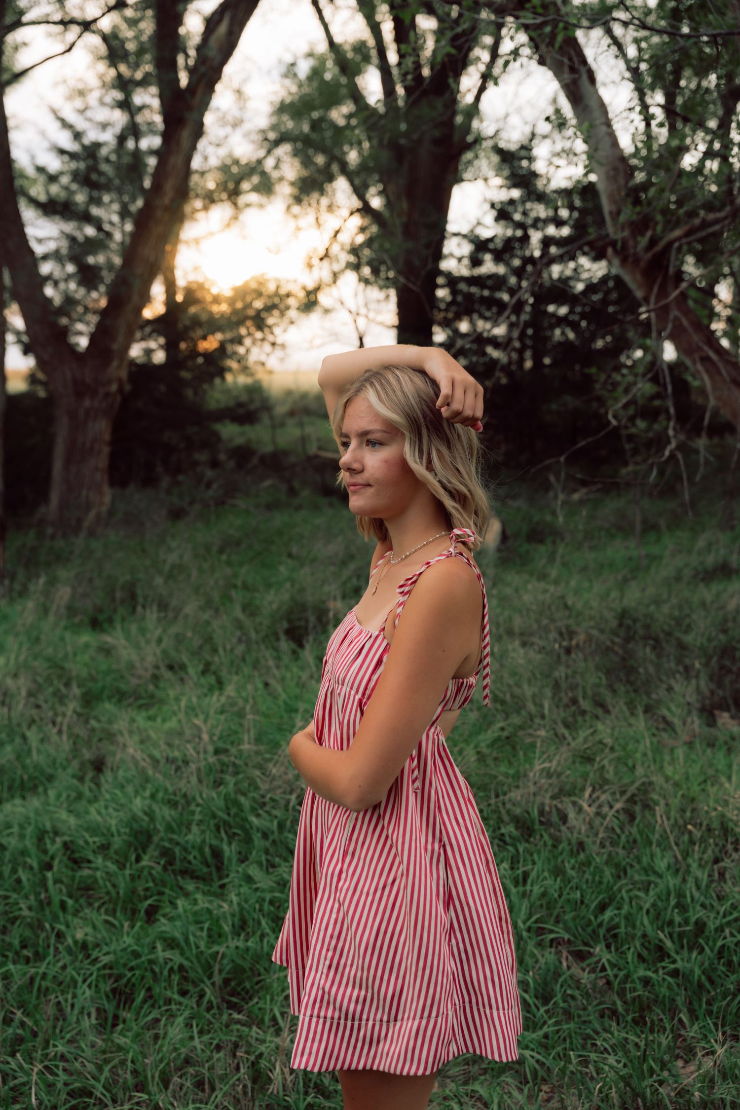 Person in striped sundress poses in natural outdoor setting during golden hour.