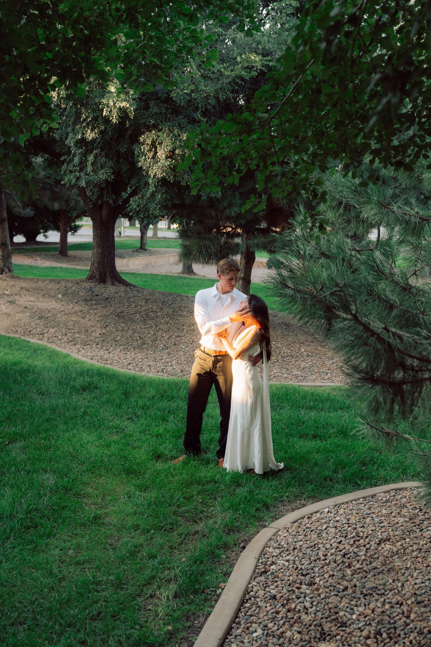 Couple embraces on a winding garden path surrounded by lush greenery.