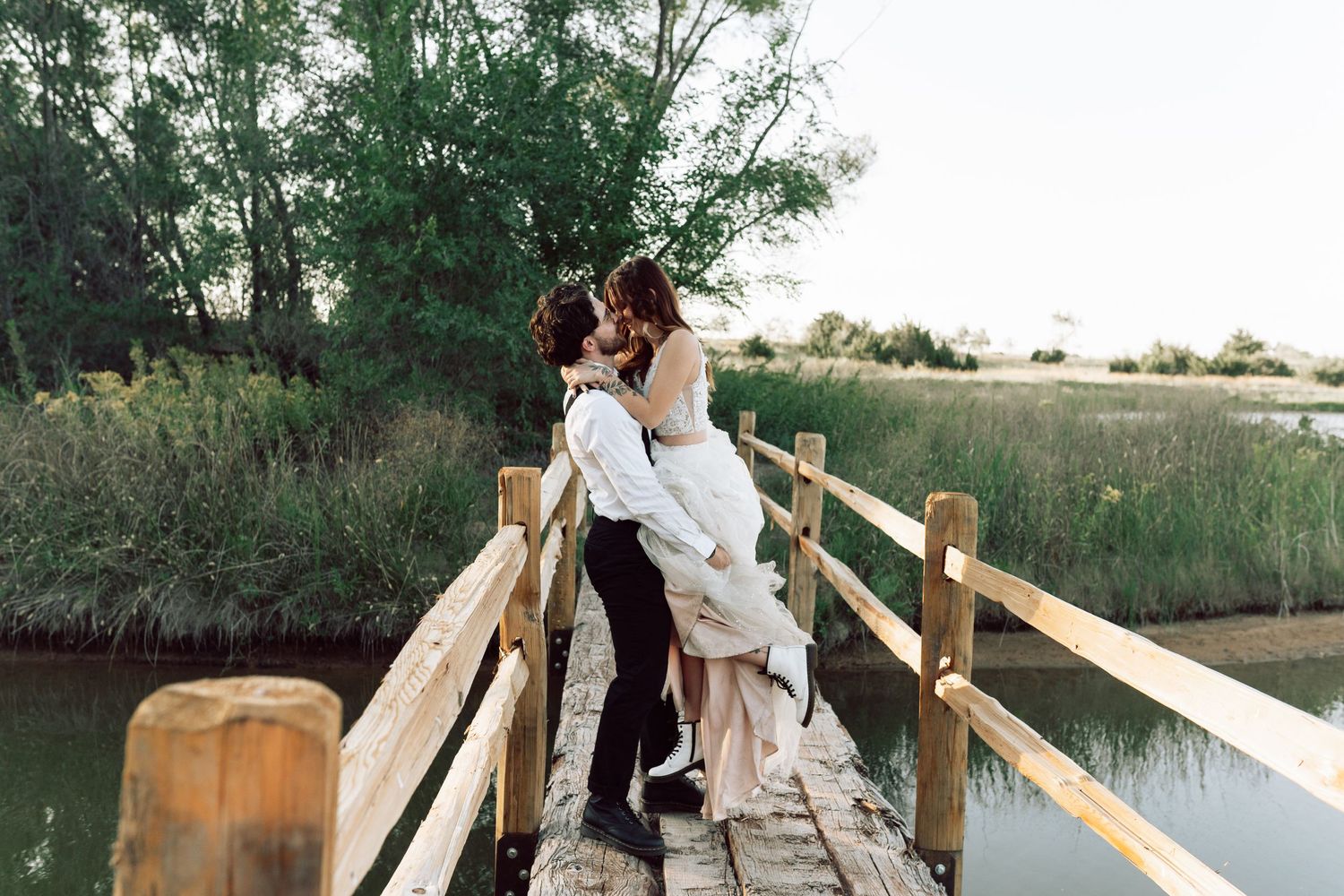 A couple embraces while standing on a rustic wooden bridge during golden hour.
