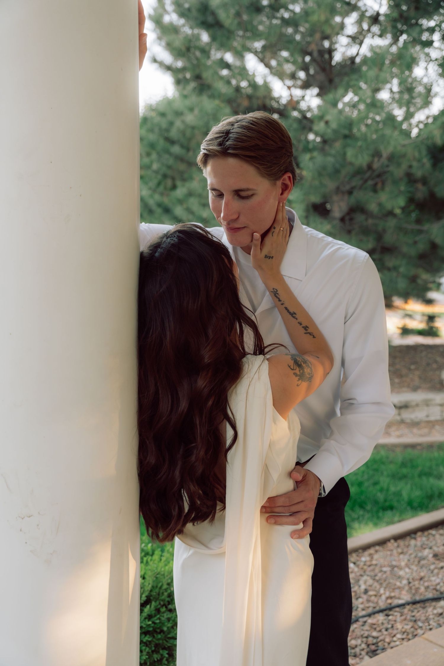 An intimate moment shared between a couple in white attire against a garden backdrop.