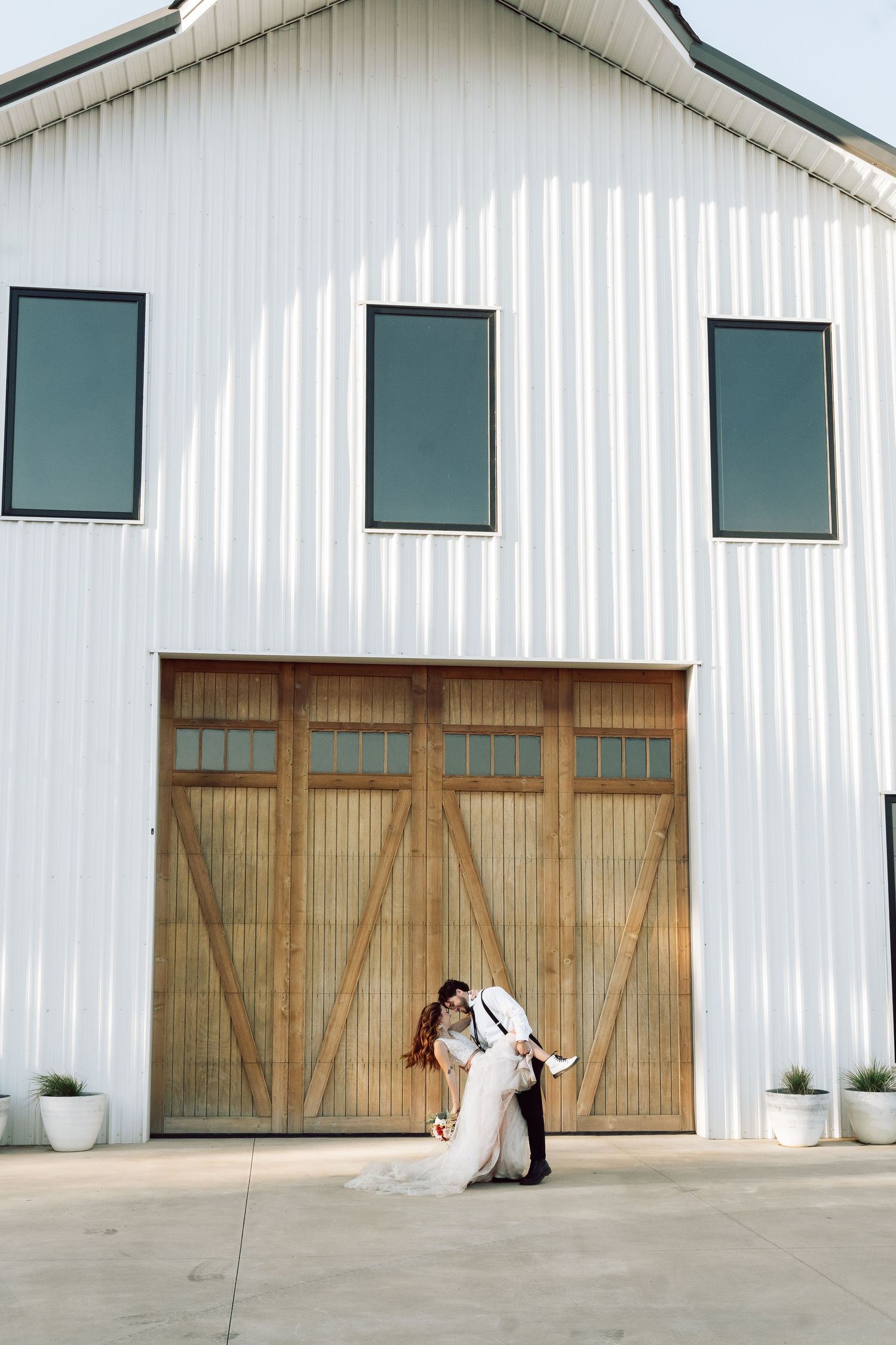 White modern barn venue with rustic wooden doors and decorative planters.