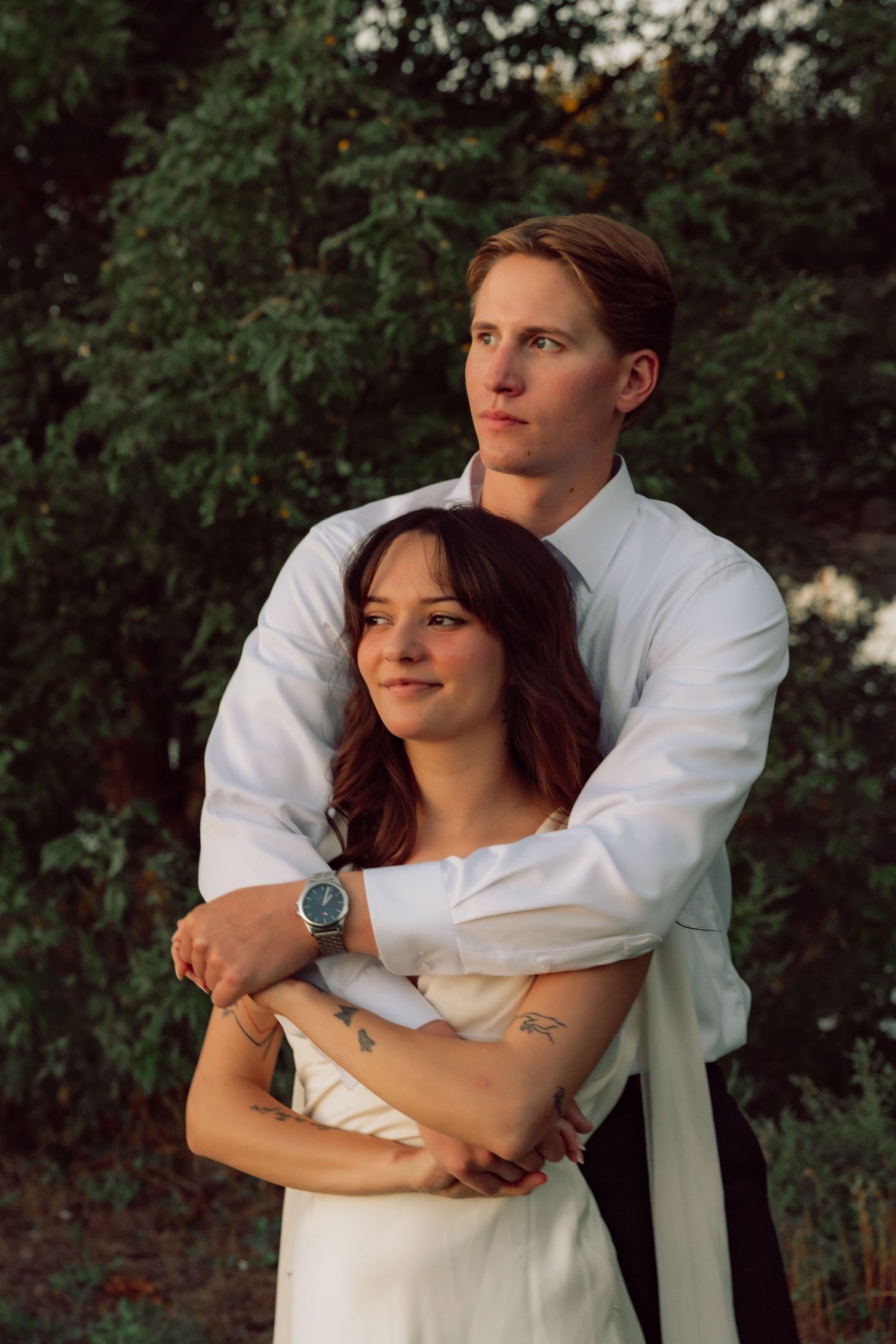 A tender embrace between newlyweds against a backdrop of green foliage at sunset.