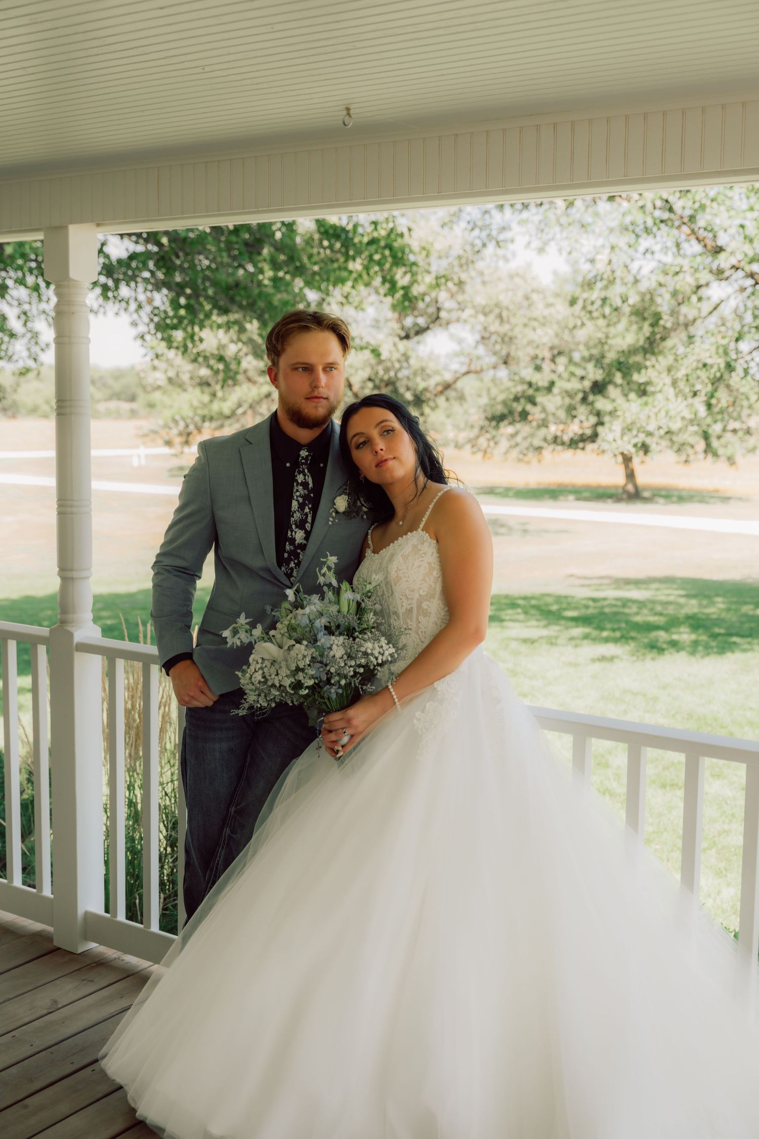 A romantic wedding portrait of a couple on a porch, with the bride in white and groom in sage green.