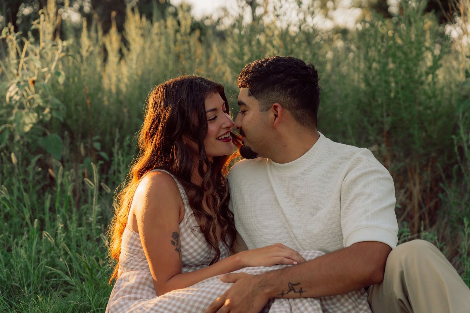 A couple shares an intimate moment while sitting together in tall grass during sunset.
