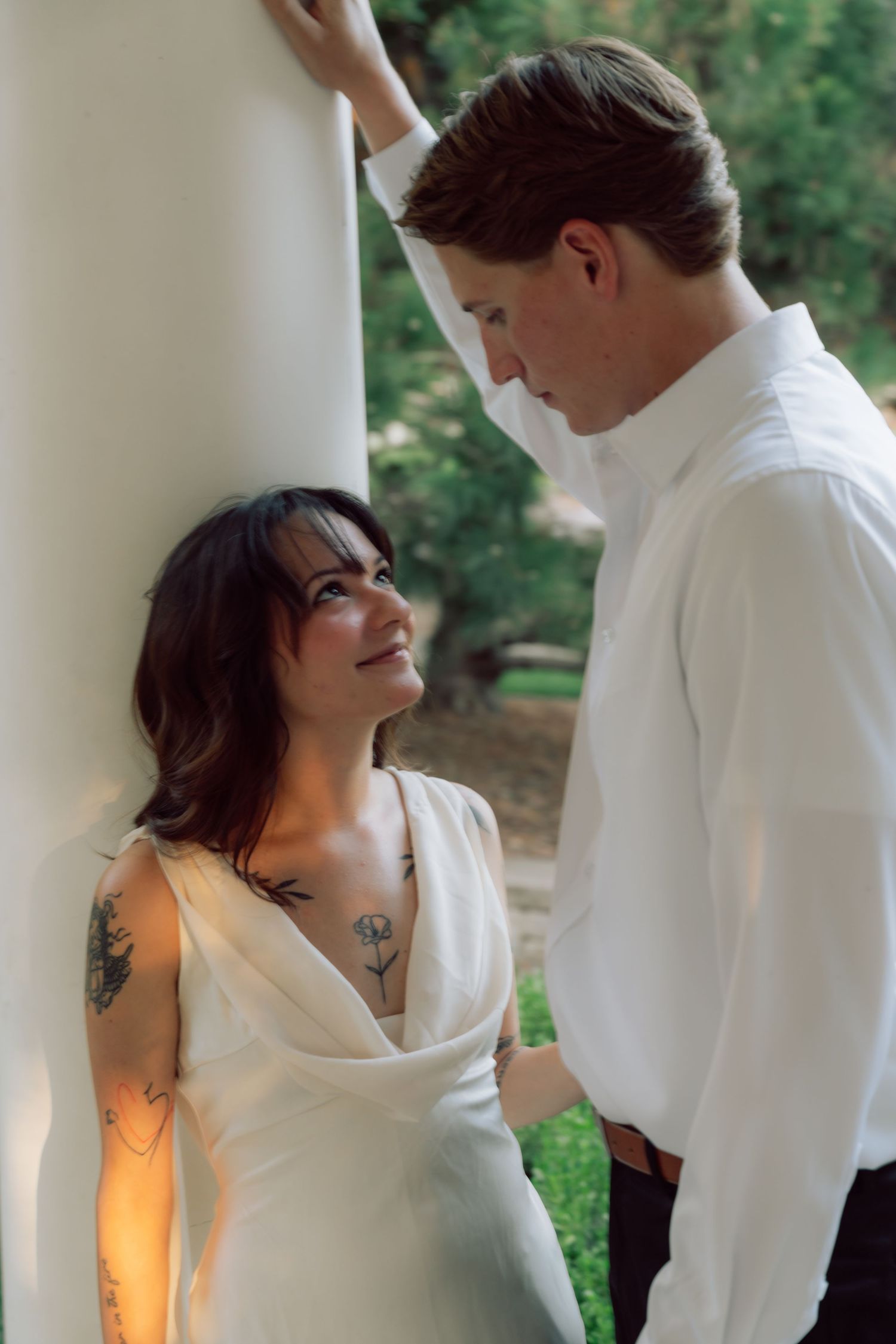 A romantic moment captured between a couple against a white column with warm sunset lighting.