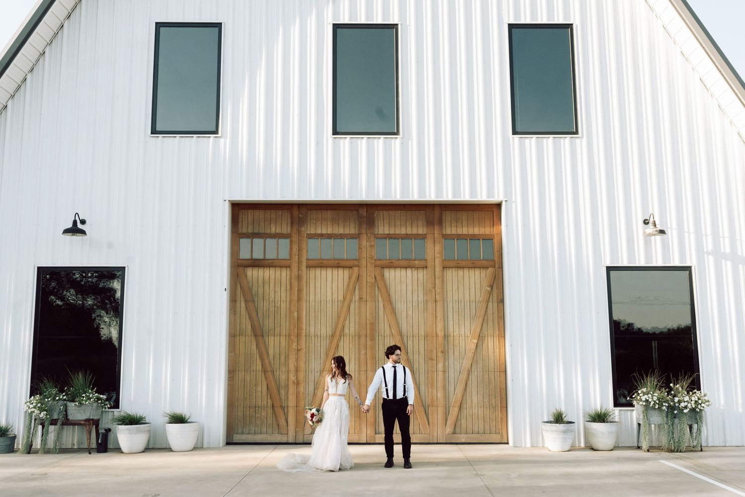A modern white barn-style building with wooden doors and windows against a blue sky.