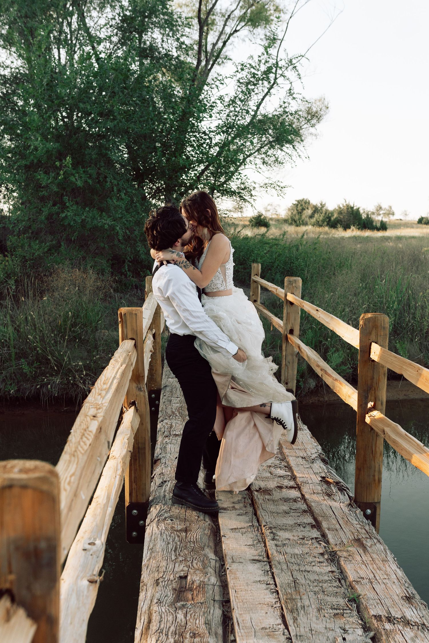 A romantic moment captured on a rustic wooden bridge surrounded by trees and water.
