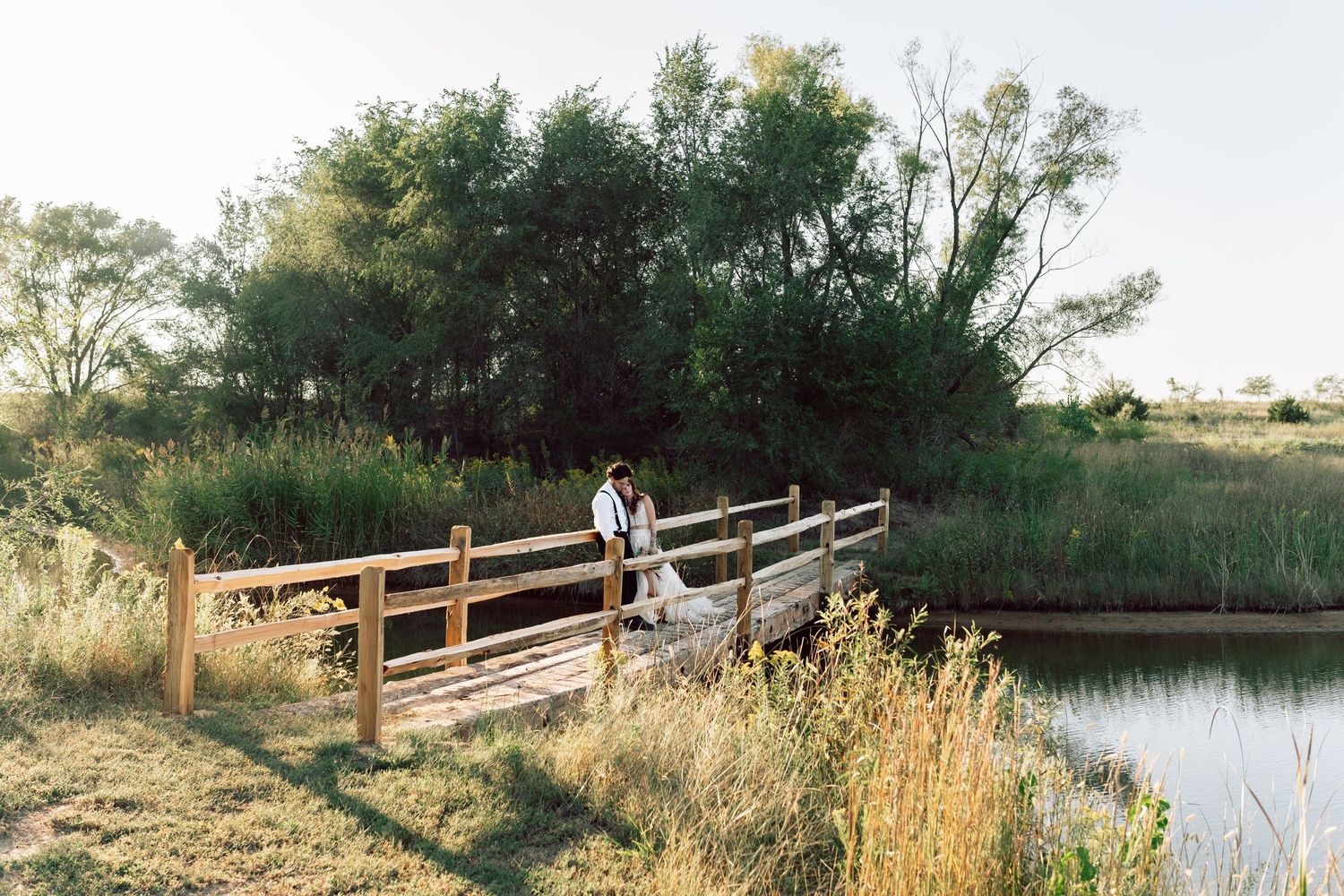 Scenic wooden footbridge stretches over tranquil pond with trees reflecting in water at dusk.