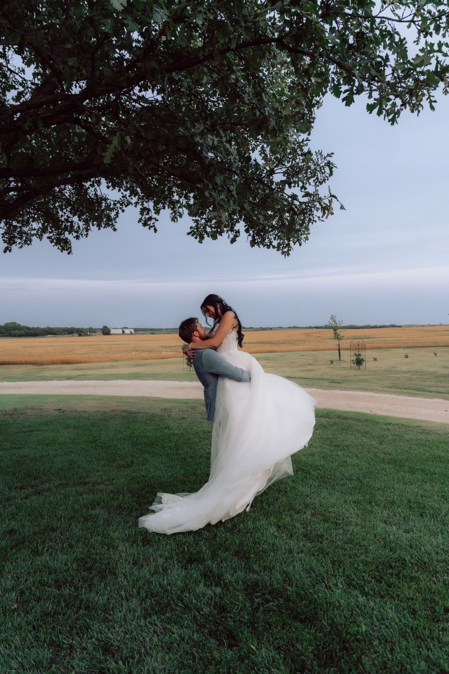 A joyful wedding couple embracing on a grassy hill against a dramatic sky.