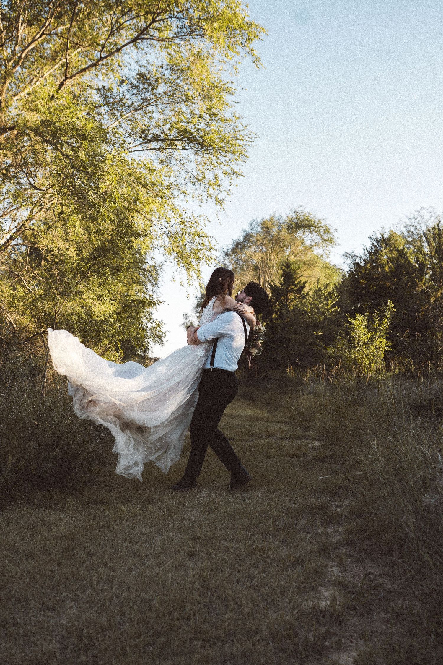 A flowing white wedding dress twirls dramatically against a natural outdoor backdrop.
