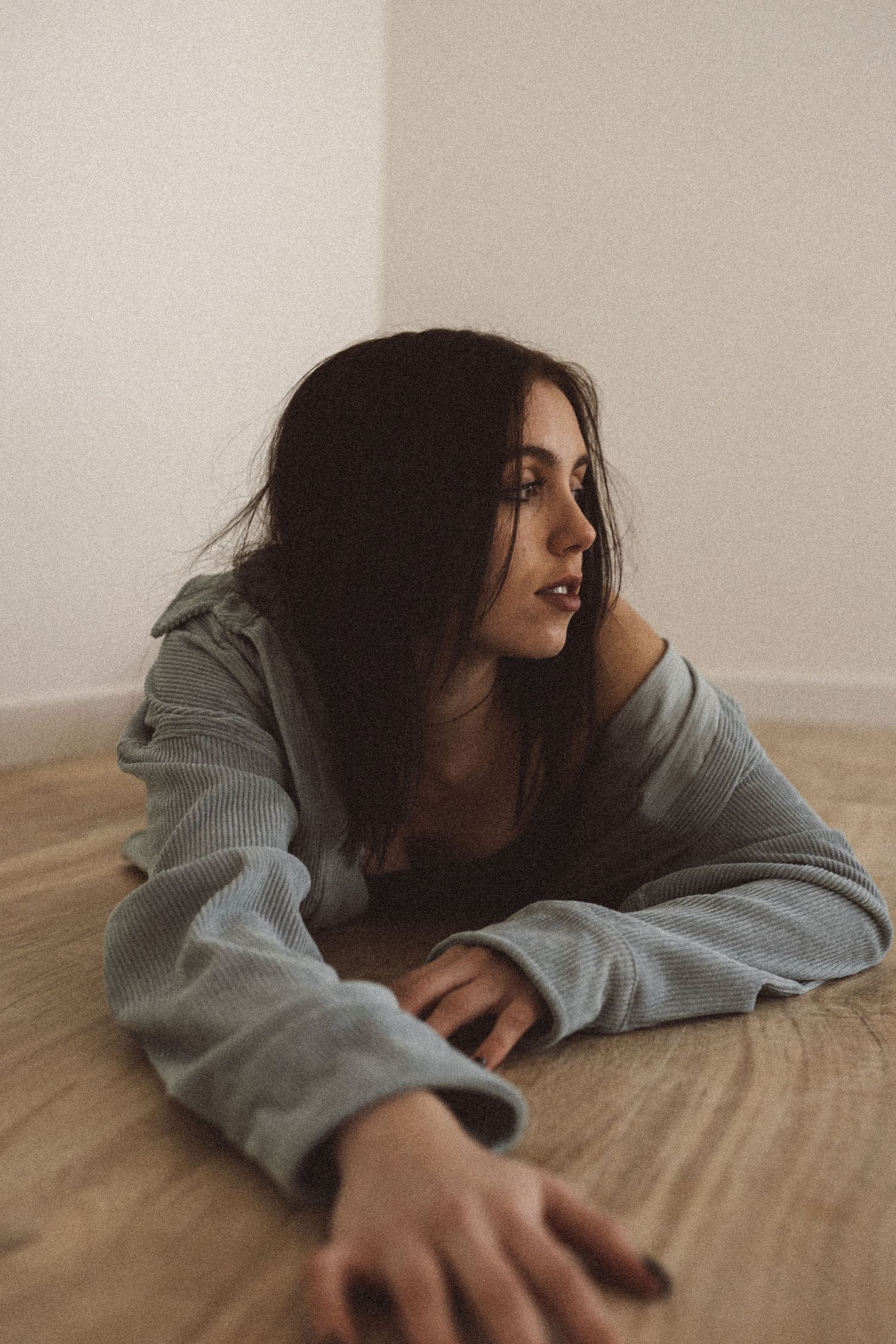 Person in gray sweater lying on wooden floor in minimalist white room.