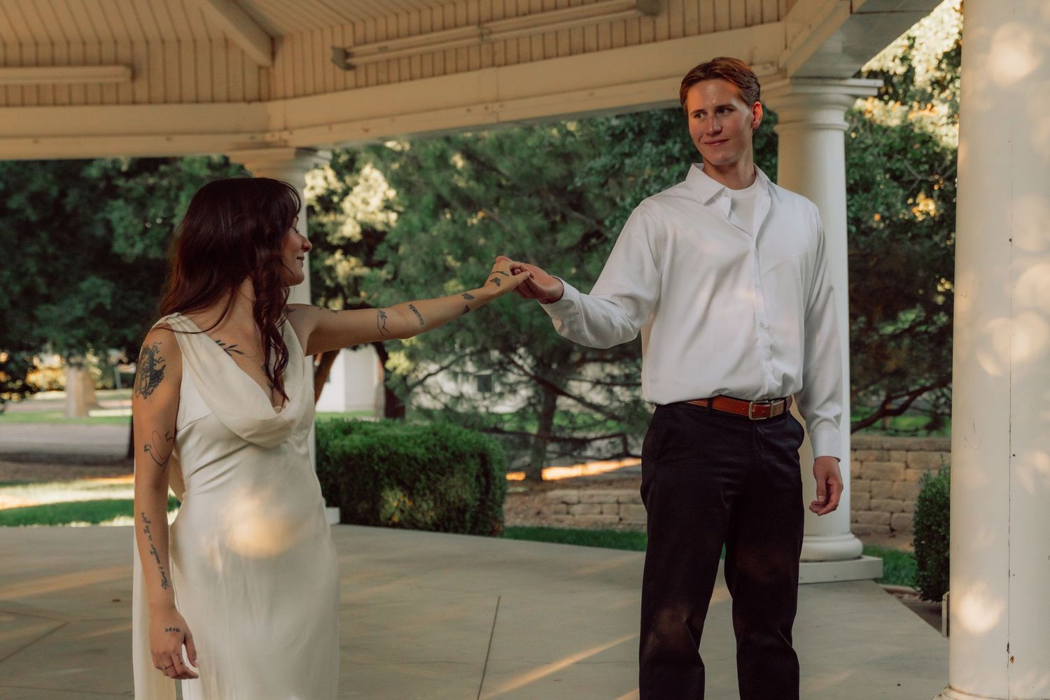 A couple in formal wear holds hands while dancing in a gazebo.