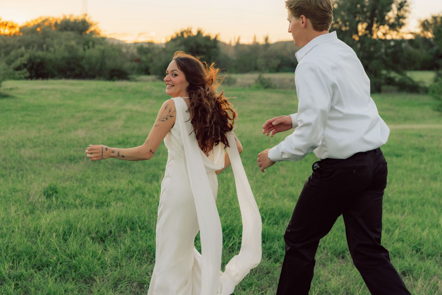 A joyful couple dances in a sunlit field, with the bride's dress flowing in the breeze.