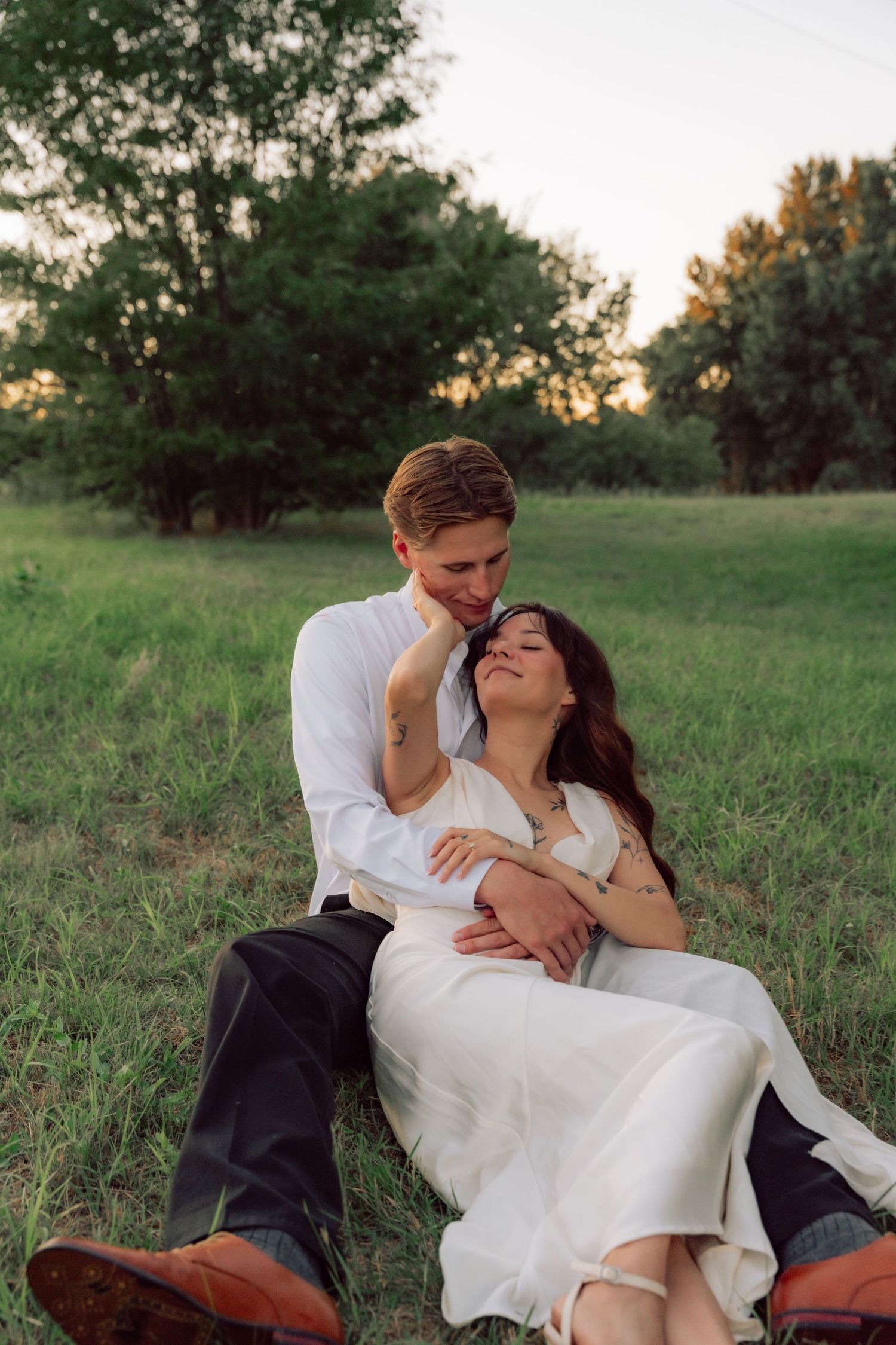 A romantic sunset moment as newlyweds relax together in a grassy field.