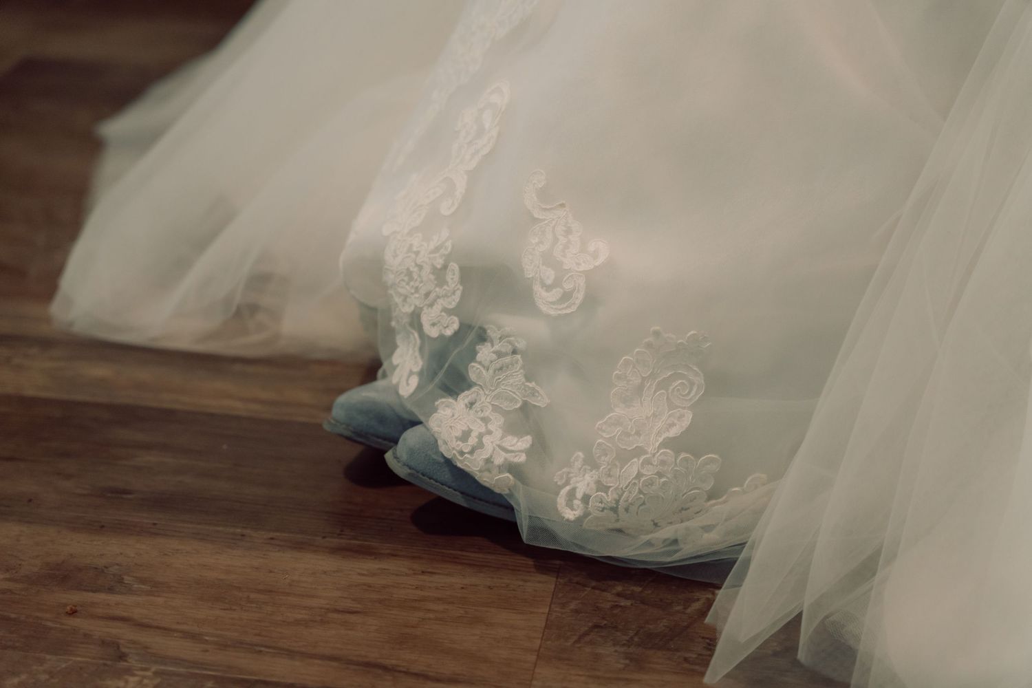 Delicate lace and tulle details of a white wedding gown spread across wooden flooring.