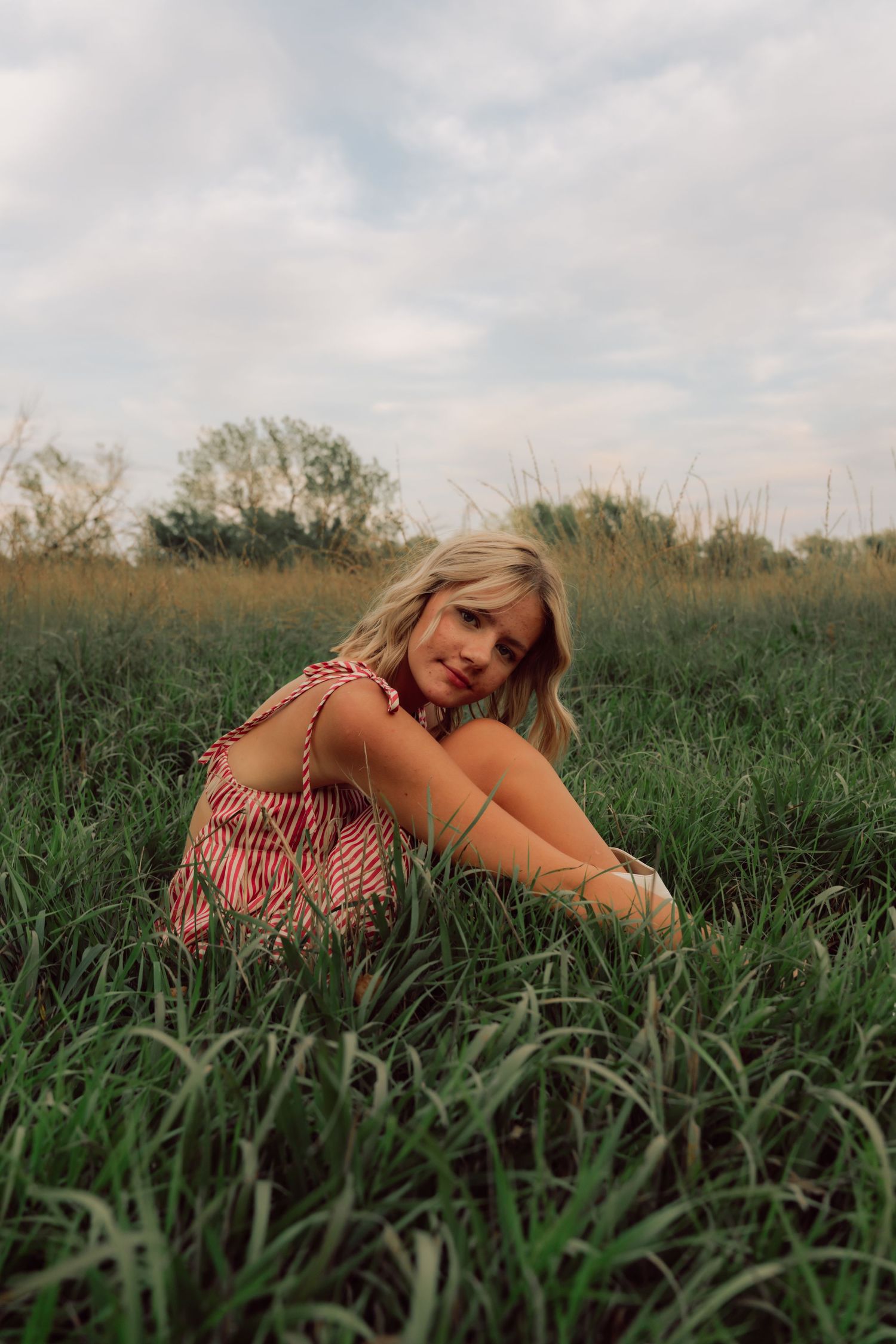 A woman in a red striped dress poses gracefully in tall green grass.