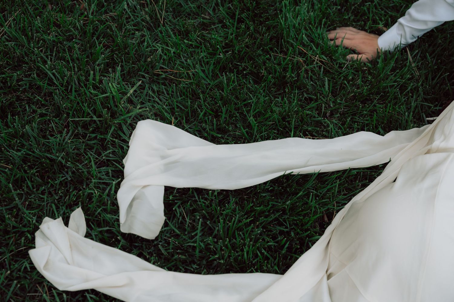 Close-up details of flowing white fabric against grass in an outdoor setting.