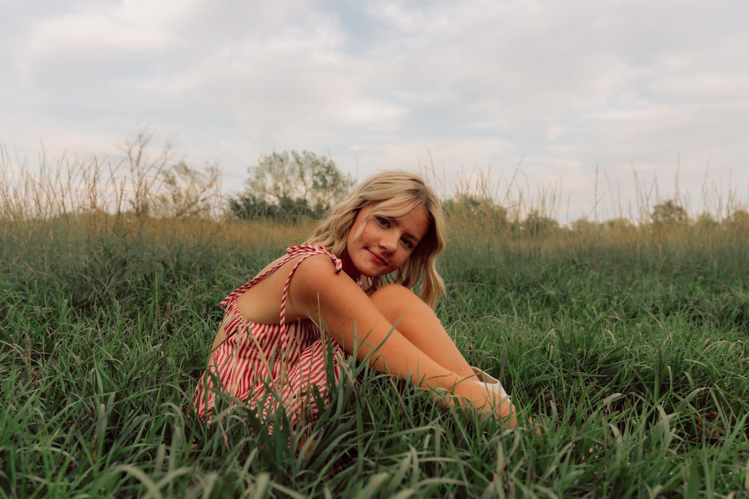 Person relaxing in tall grass wearing summer attire during outdoor photoshoot.